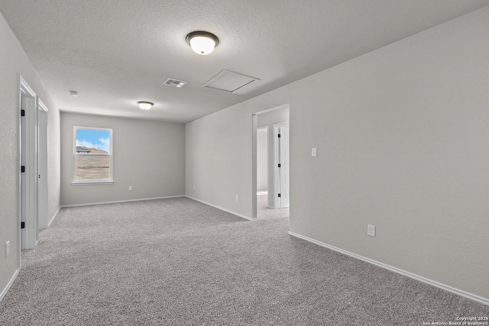 Spacious upstairs bonus room with gray carpet, neutral walls, multiple doorways, and natural light in 5-bedroom The Brazos C home, San Antonio