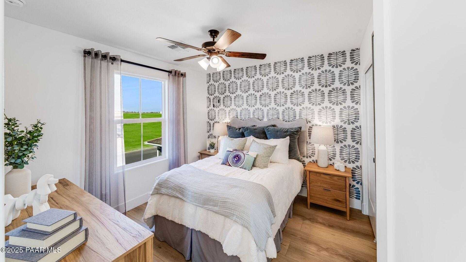 Cozy bedroom with patterned accent wall, queen bed in gray linens, window view of green field, wooden desk in Davidson Homes Wilmington B, Prescott AZ