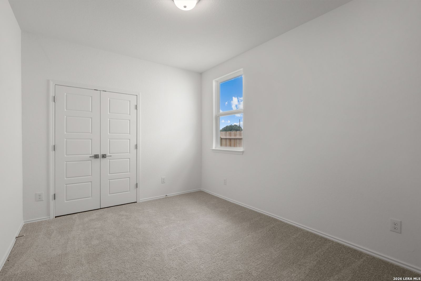 Bright secondary bedroom with white walls, beige carpet, double closet doors, and window view of backyard in The Glenwood E, Elmendorf, Texas