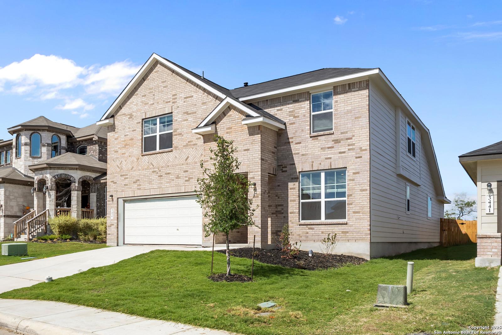 Two-story brick Davidson Homes Sequoia A with 2-car garage, driveway, young tree, and lush green lawn in Horizon Pointe, Converse, TX