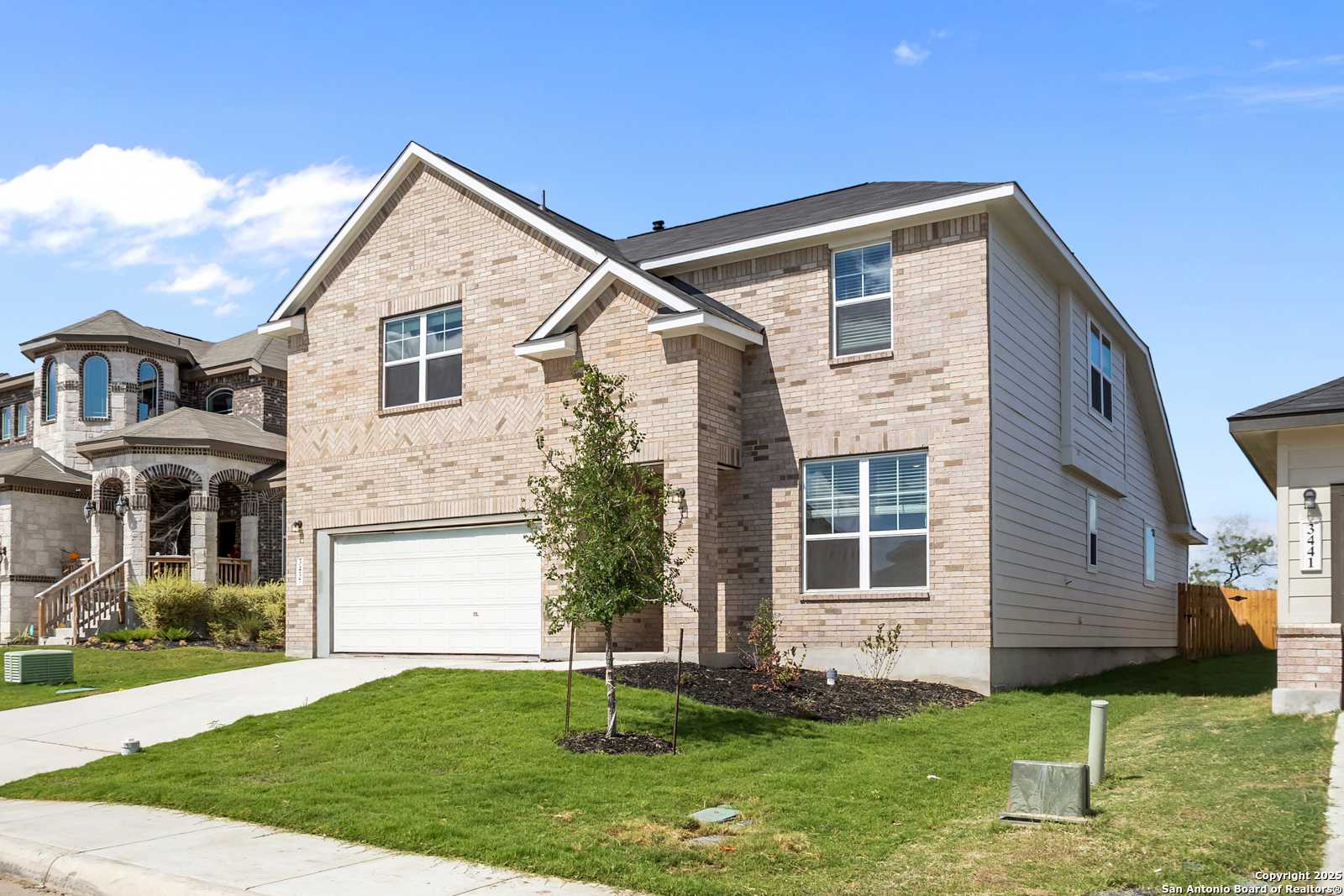 Two-story brick Davidson Homes Sequoia A with 2-car garage, driveway, young tree, and lush green lawn in Horizon Pointe, Converse, TX