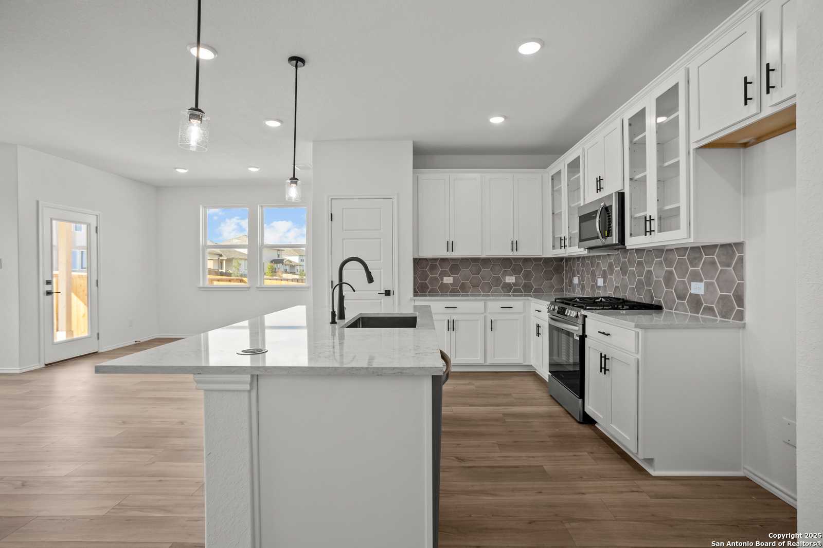 Modern white kitchen with quartz island, stainless appliances, hex tile backsplash in Davidson Homes The Daphne K, San Antonio