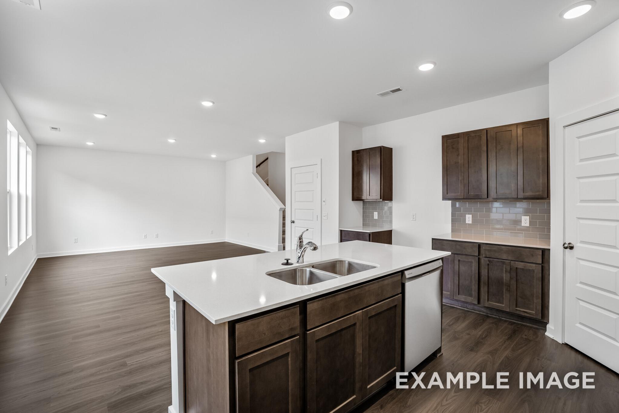 Spacious open-concept kitchen in The Logan C home design featuring white quartz island, shaker cabinets, hardwood floors