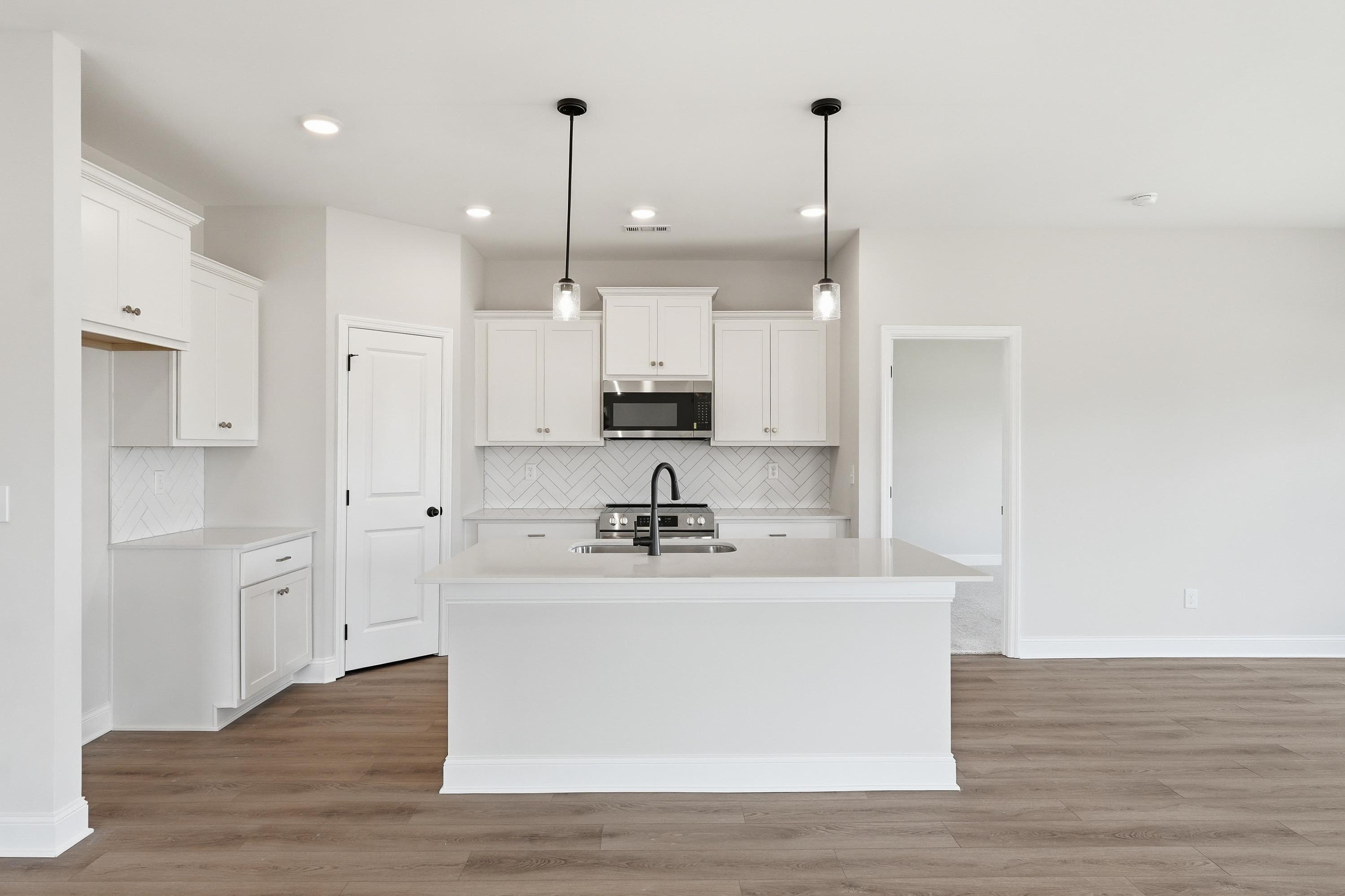 Modern kitchen in The Glen A featuring white cabinets, a central island, herringbone backsplash, and wood-style flooring.