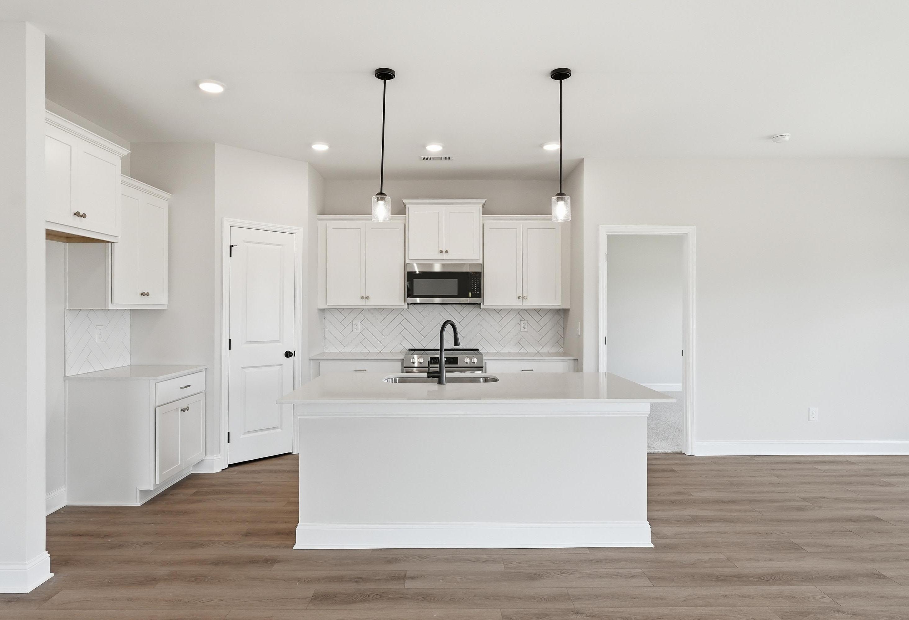 Modern kitchen in The Glen A featuring white cabinets, a central island, herringbone backsplash, and wood-style flooring.