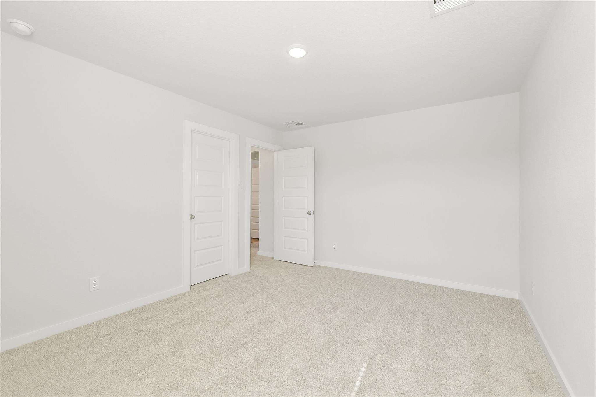 Bright secondary bedroom with white walls, beige carpet, and double doors in Davidson Homes San Marcos E, Cleveland TX