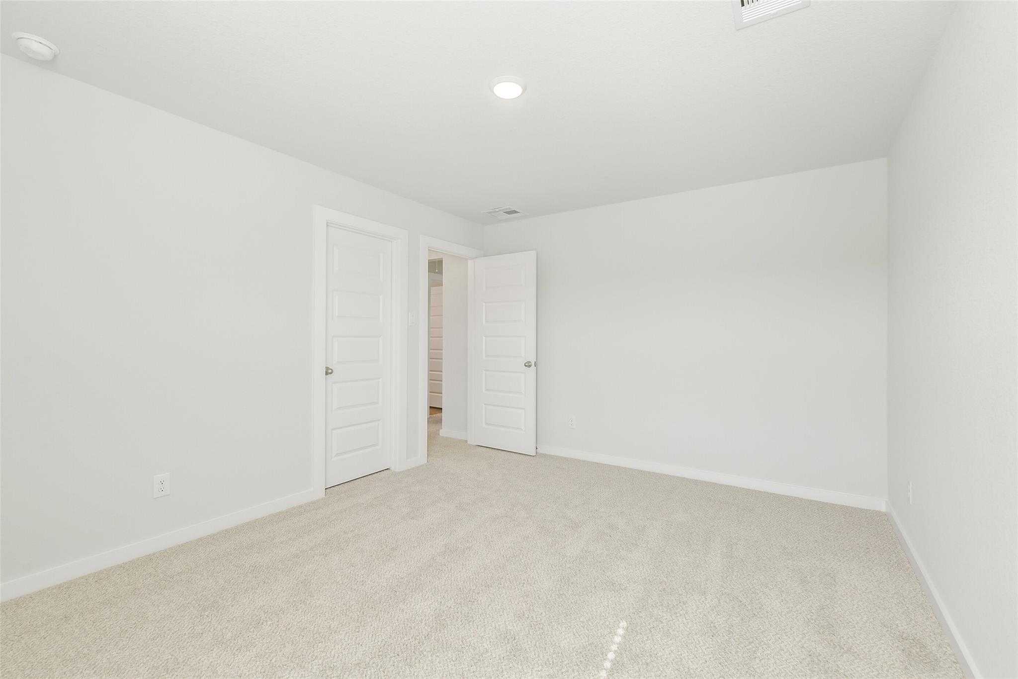 Bright secondary bedroom with white walls, beige carpet, and double doors in Davidson Homes San Marcos E, Cleveland TX