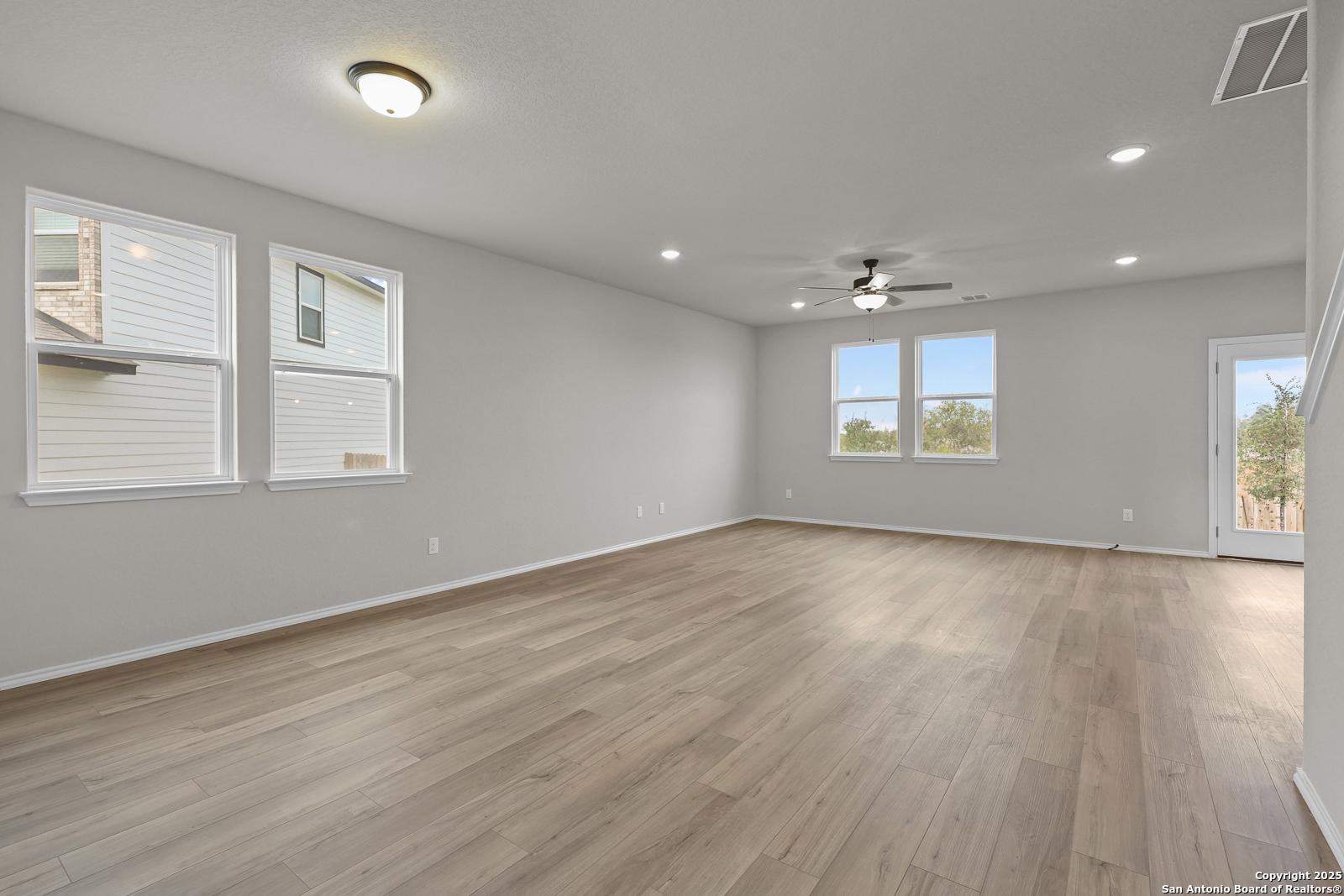 Spacious living room with light gray walls, hardwood floors, large windows, ceiling fan, and sliding door in Davidson Homes The Murray J, San Antonio