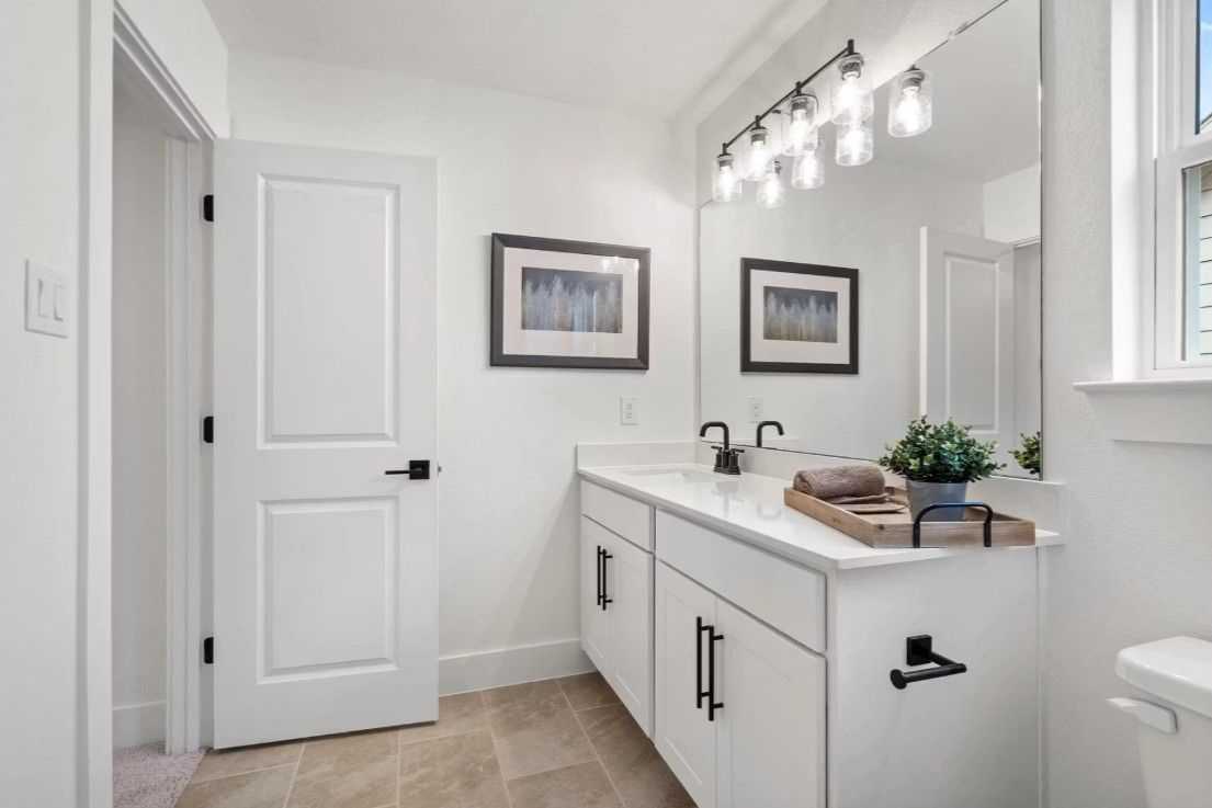 Bright modern bathroom with white double vanity, large mirror, pendant lights, and potted plant in Davidson Homes The Wake C, Wylie