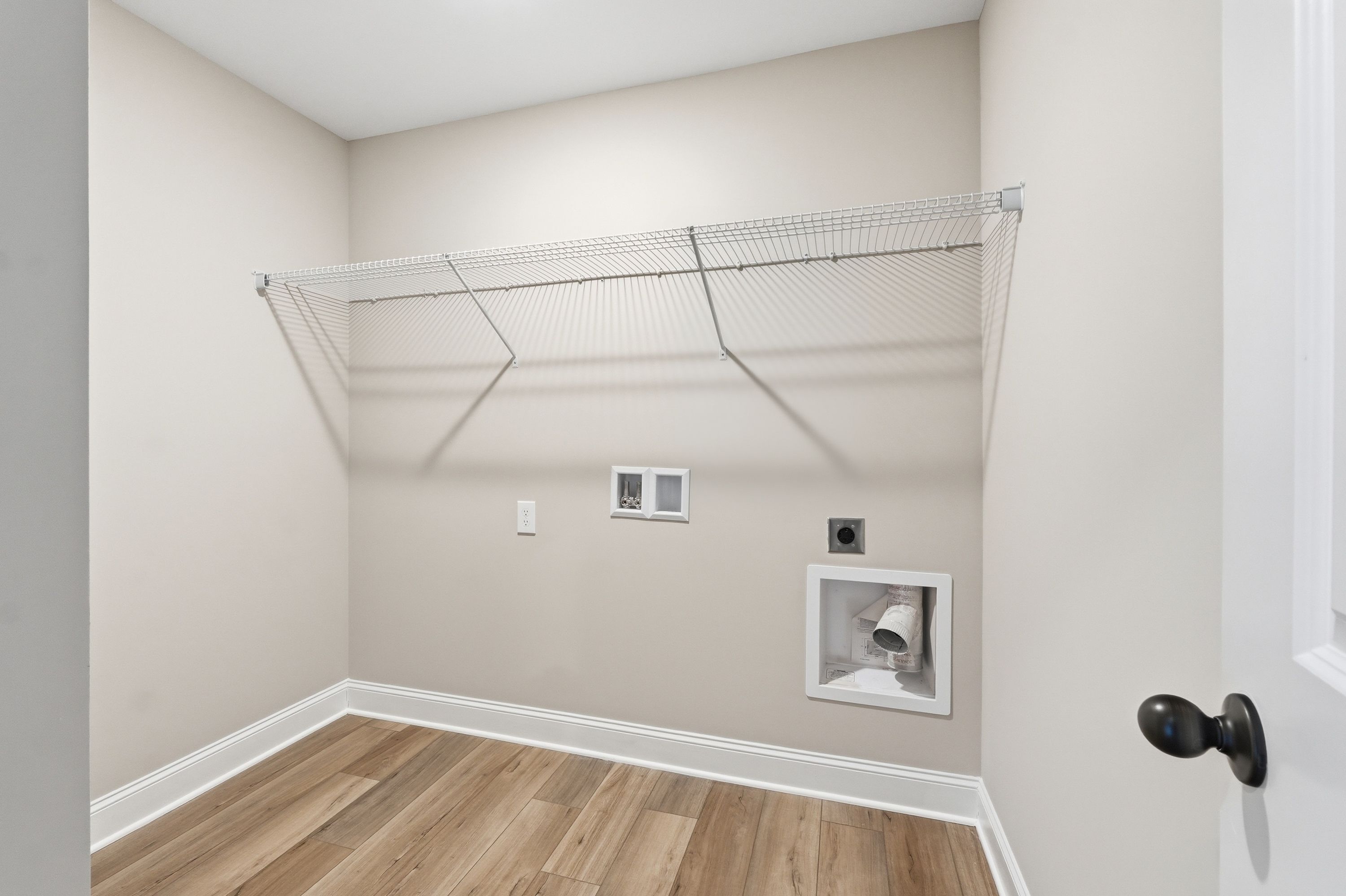 Spacious laundry room in The Daphne V with wire shelving, washer-dryer hookups, neutral beige walls, and hardwood floors