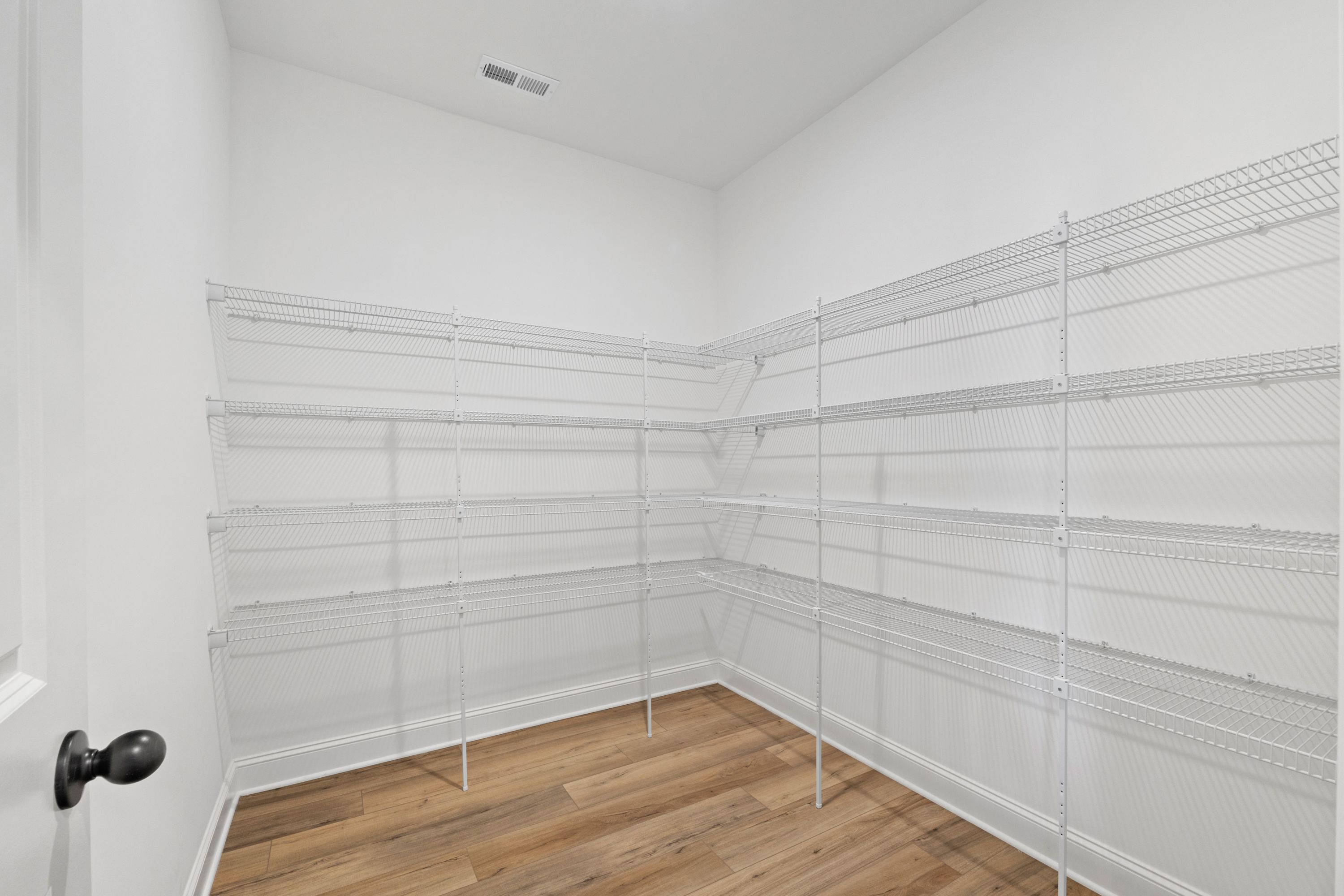 Spacious walk-in closet in The Valencia home design featuring white wire shelving and hardwood floors