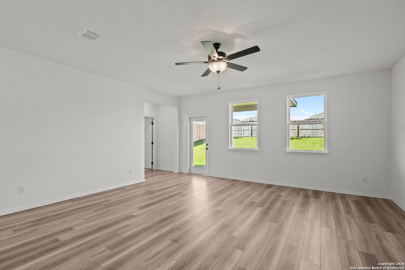 Bright living room with ceiling fan, large windows to lush backyard, hardwood floors in Davidson Homes The Douglas E, San Antonio