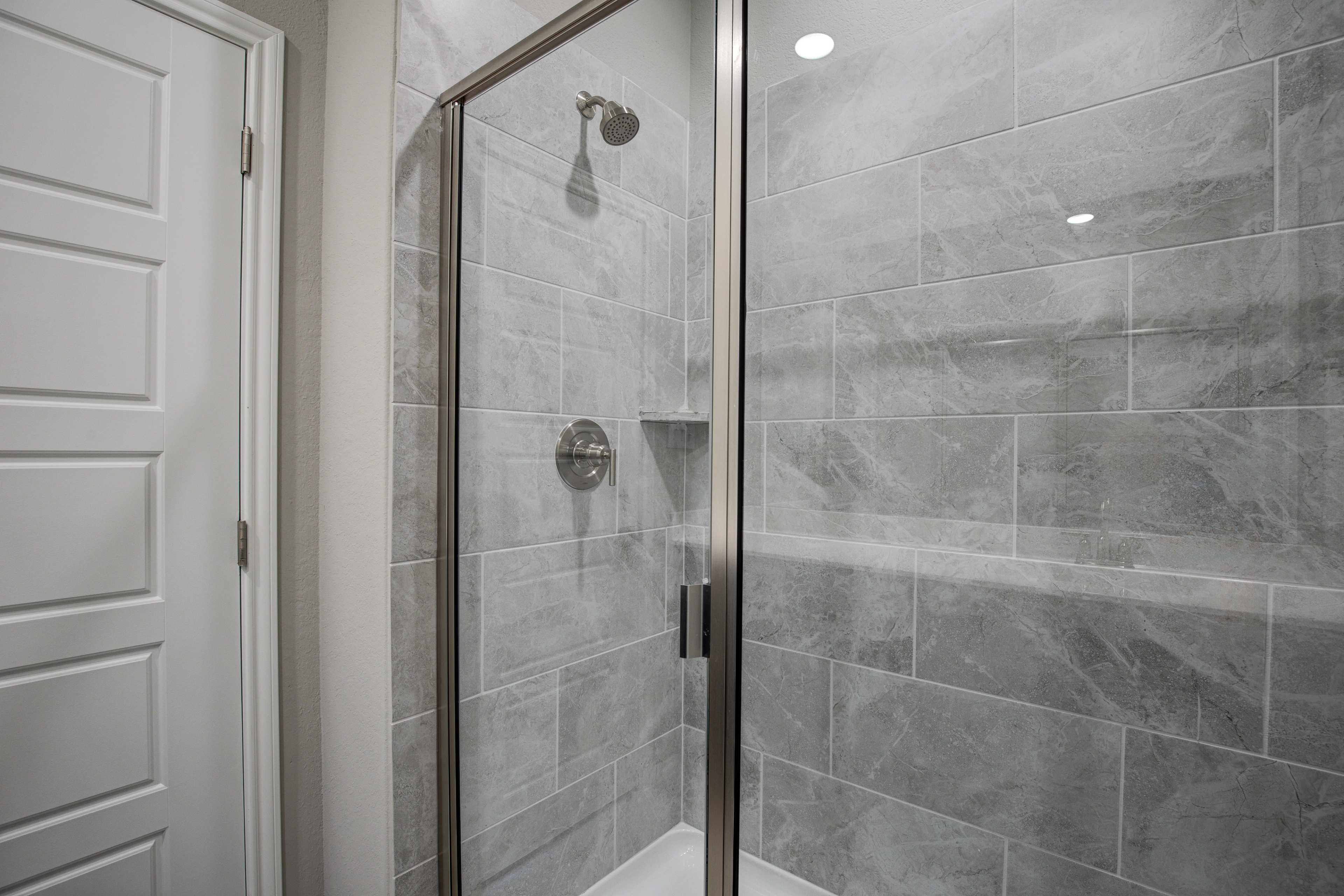 Modern frameless glass shower in The Frio B master bath featuring gray subway tile walls and built-in niche