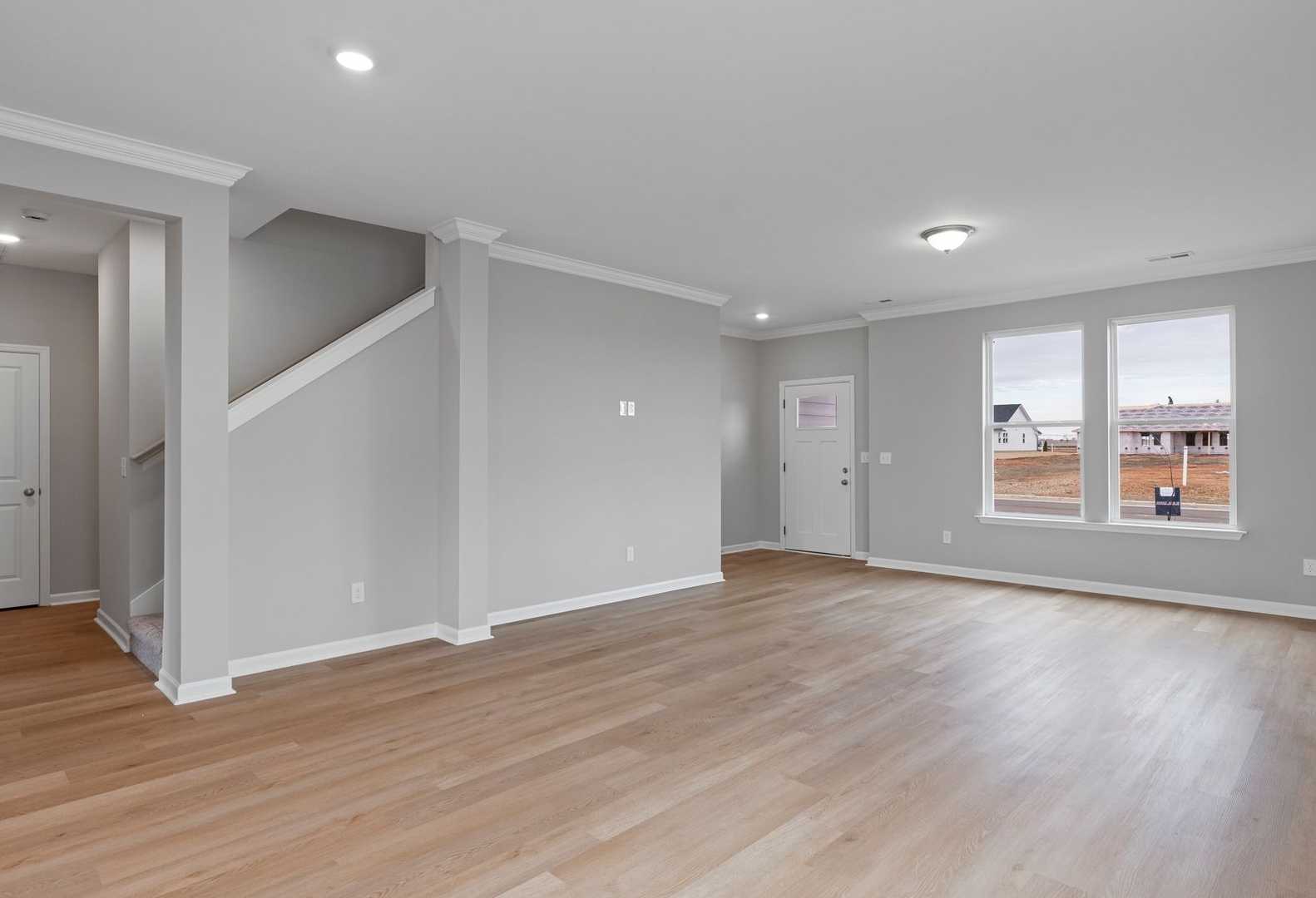 Spacious main floor living area in The Stella A with open layout, hardwood floors, gray walls, staircase, and large windows overlooking fields