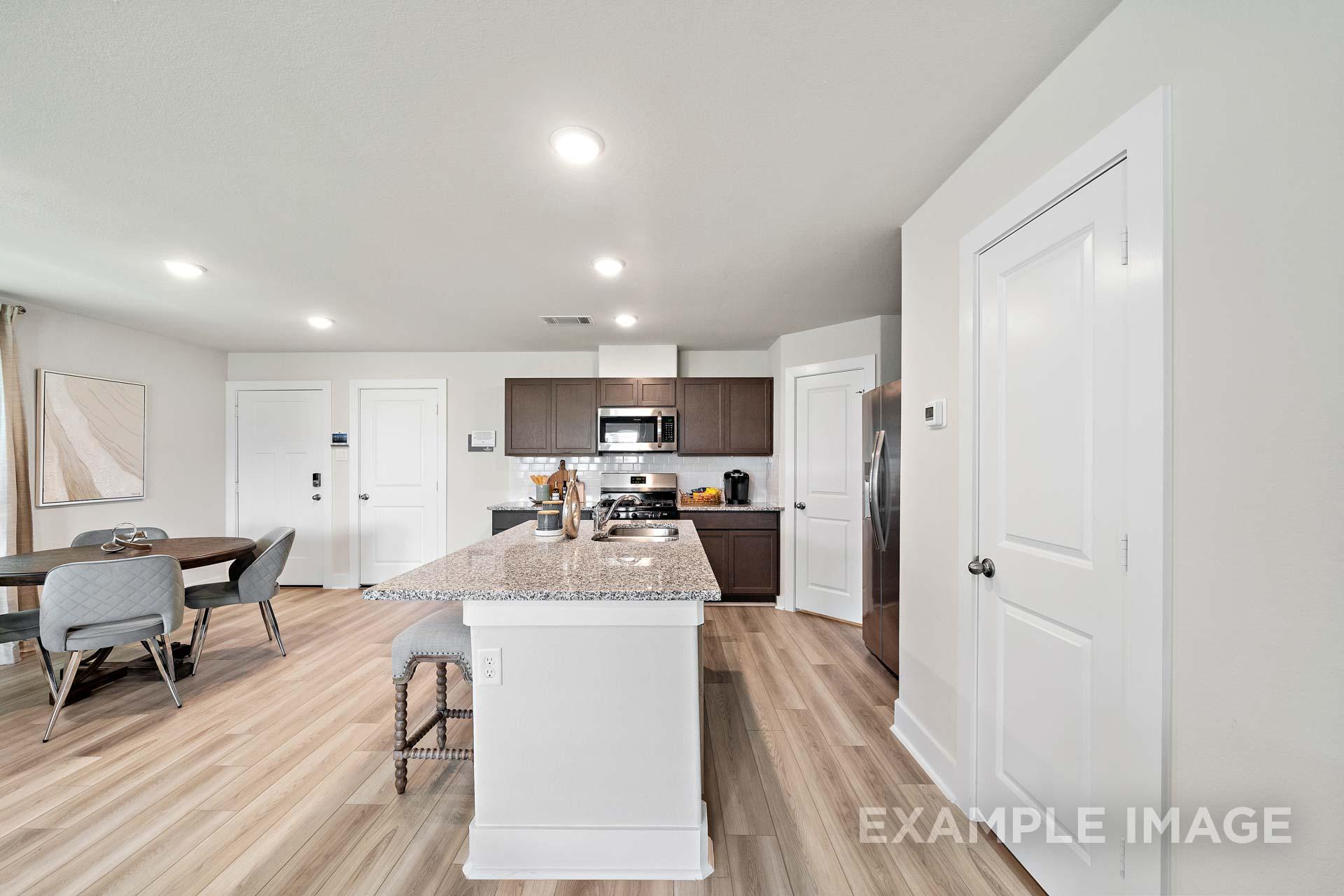 Modern open-concept kitchen in The Lily A with granite island, stainless appliances, brown cabinets, and hardwood floors