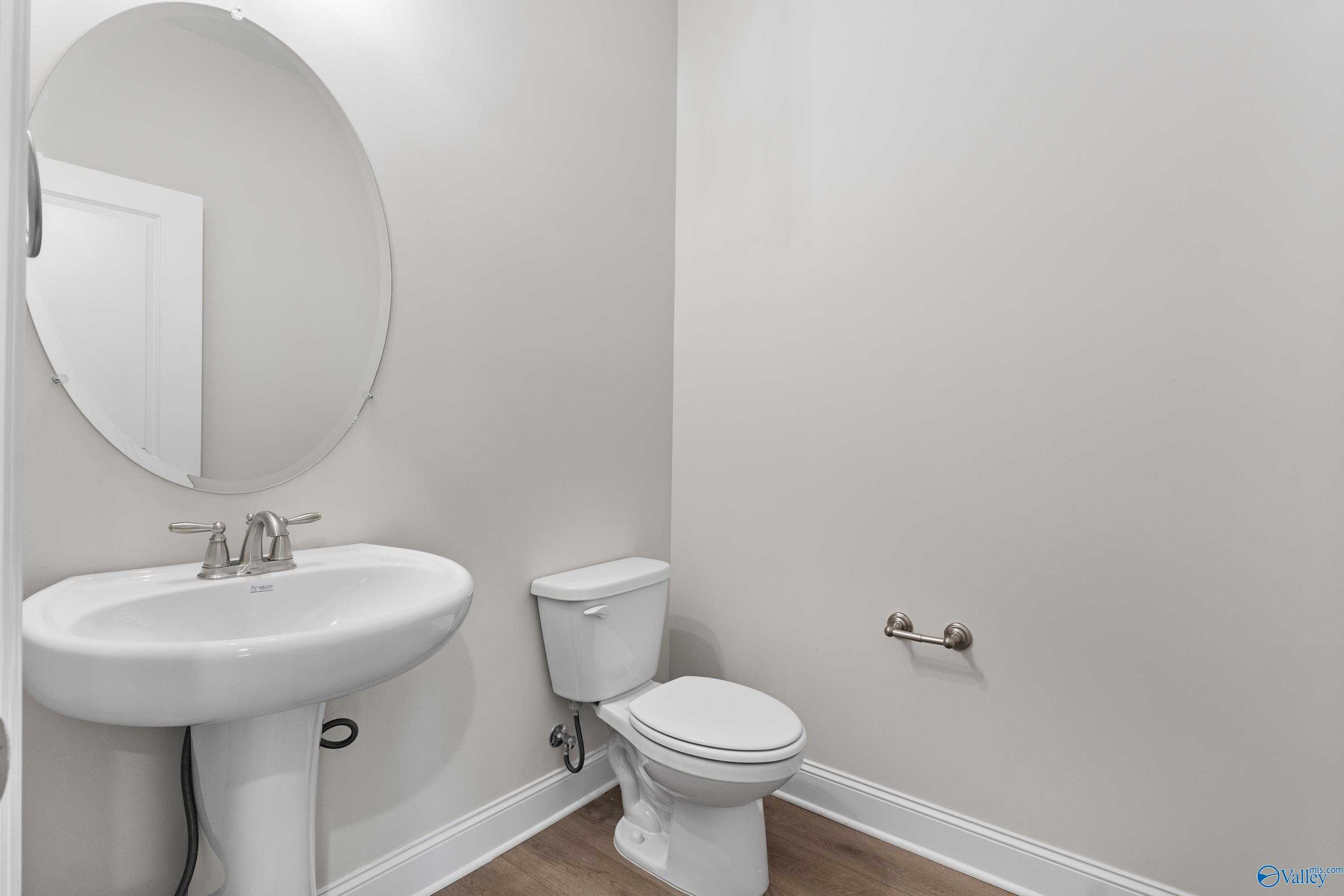 Elegant powder room with pedestal sink, round mirror, and white toilet in Davidson Homes The Finleigh, Toney, Alabama