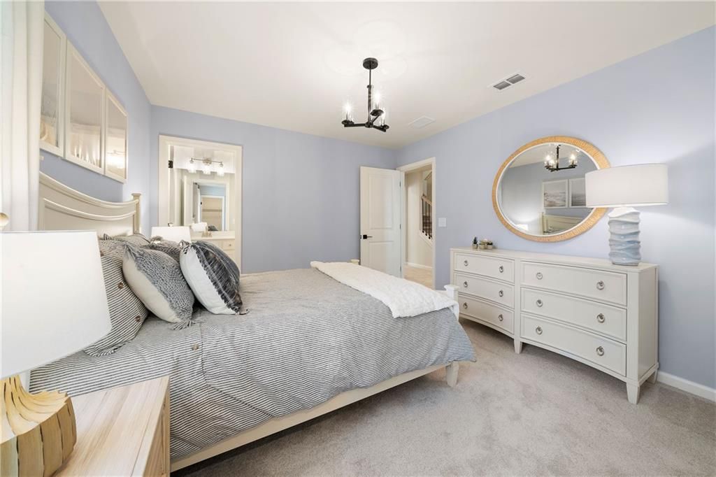 Light blue bedroom with gray striped king bed, white dresser, round mirror, chandelier in Davidson Homes Willow B, Riverwood, Dallas, GA