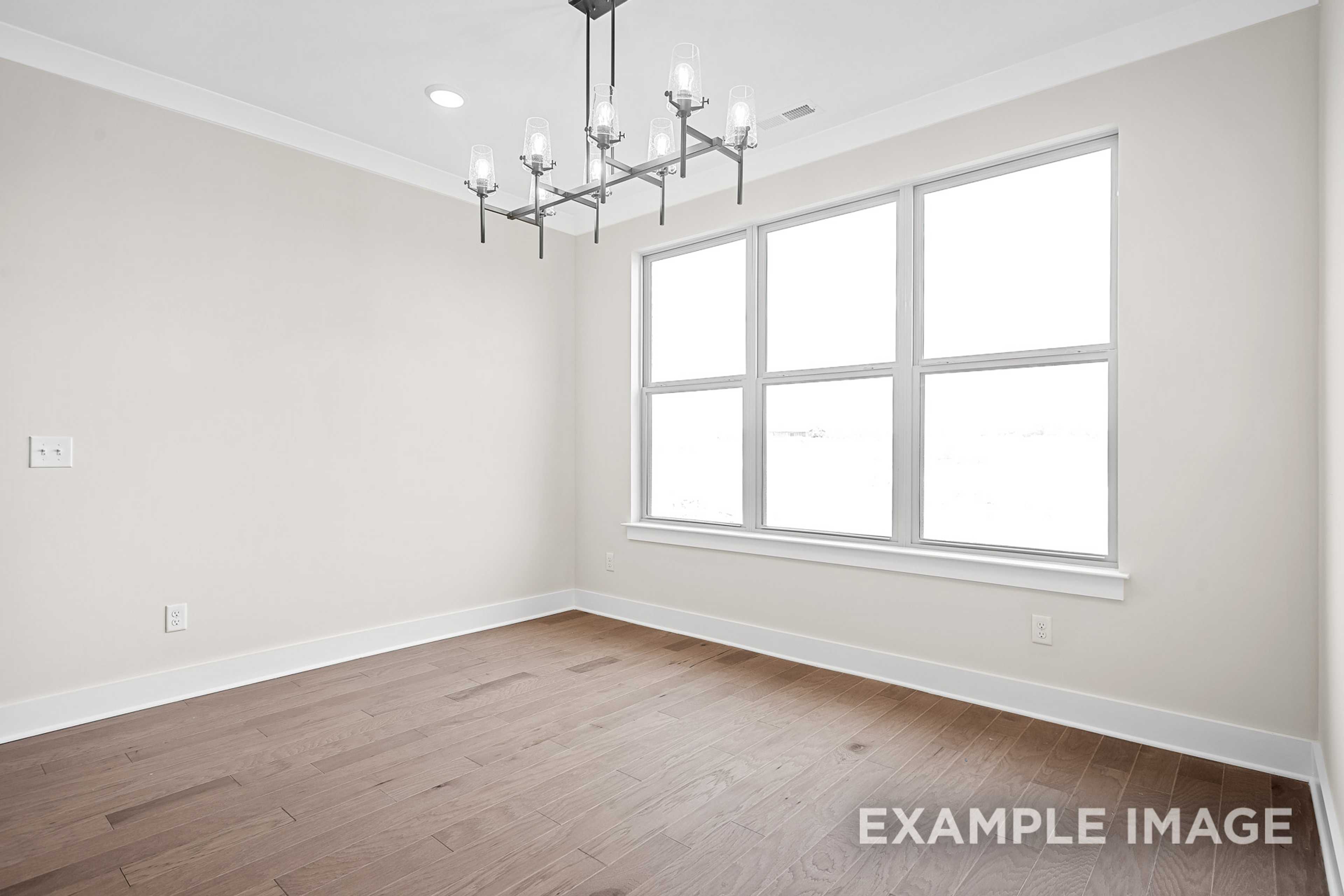 Spacious dining room in The Hawkins home design featuring hardwood floors, neutral walls, large windows, and modern chandelier