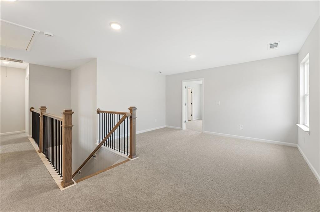 Upstairs landing with wooden balustrade staircase and carpeted open space in The Rabun C 4-bedroom home, Winder, Georgia