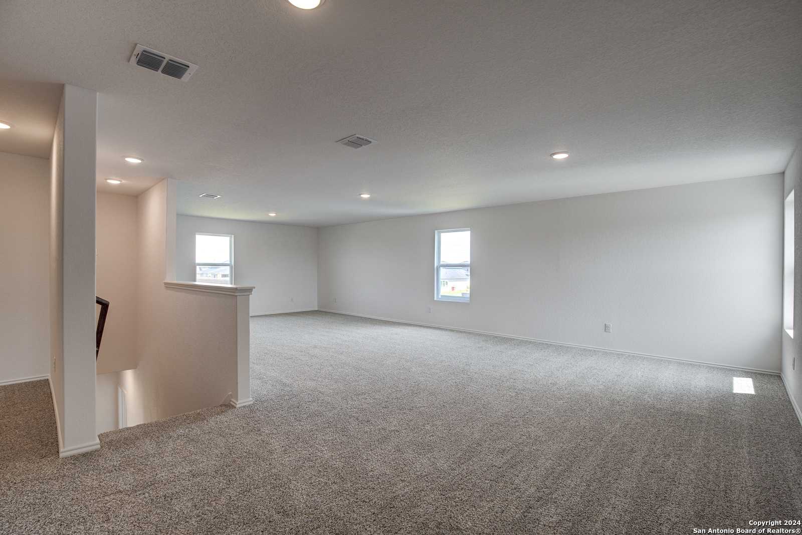 Spacious upstairs loft with plush beige carpet, white walls, and large windows in Davidson Homes The Douglas D, Seguin, Texas