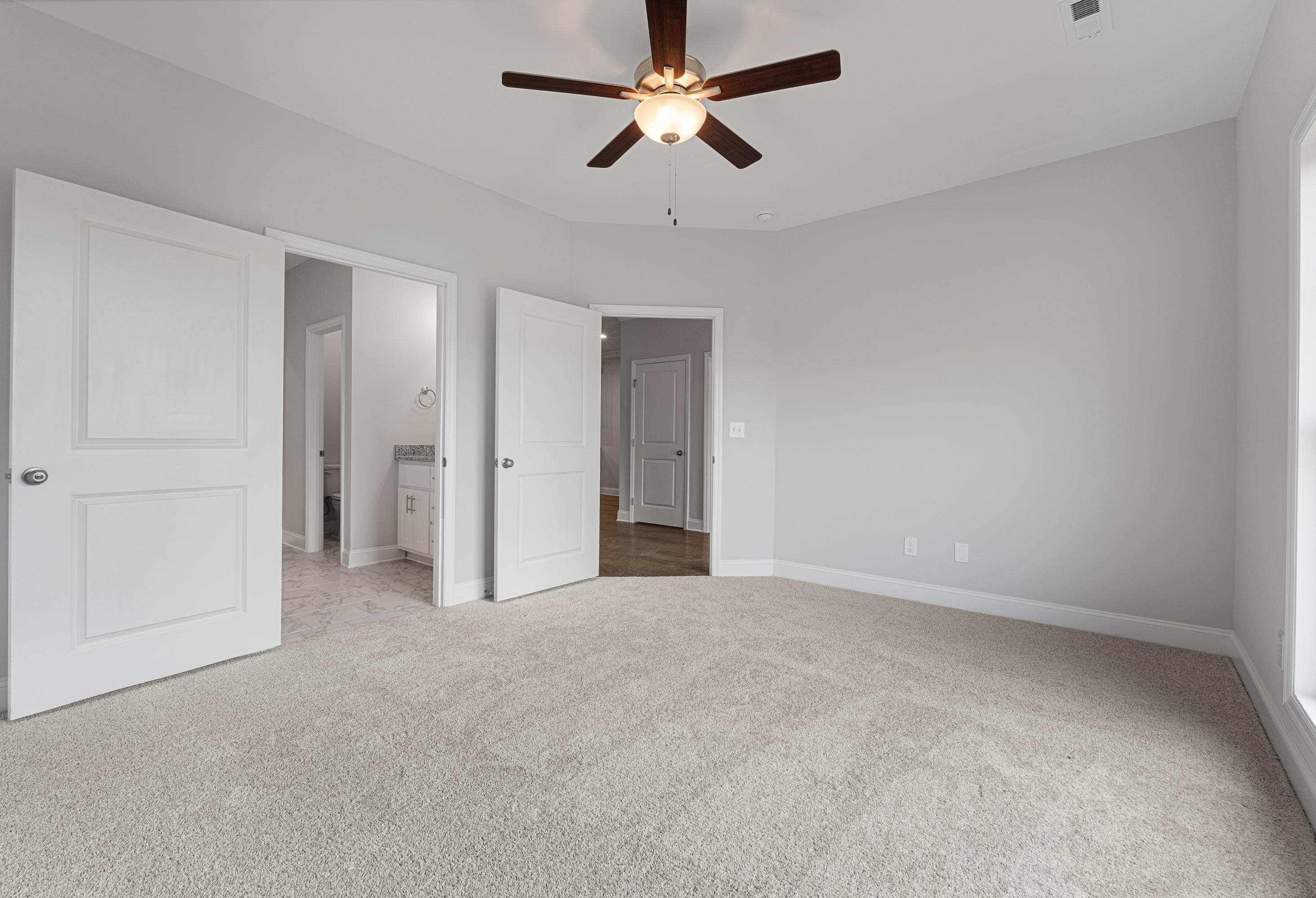 Spacious master bedroom in The Copeland B by Davidson Homes: gray walls, beige carpet, ceiling fan, open doors to en-suite bath