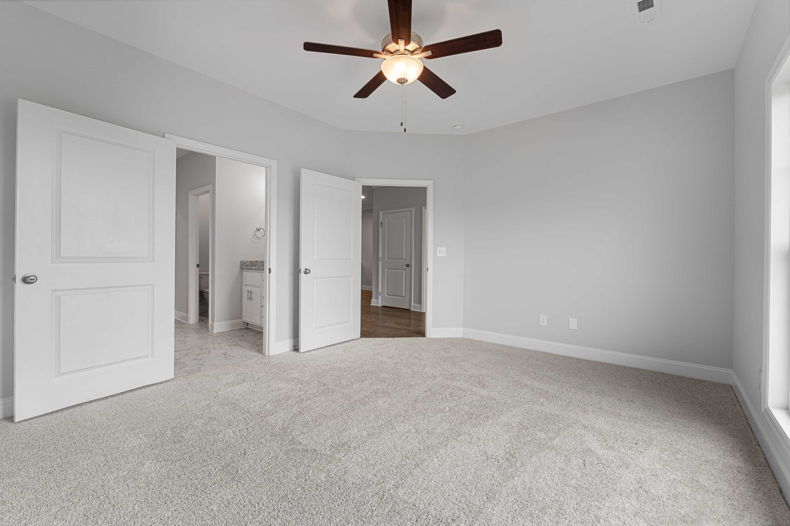 Spacious master bedroom in The Copeland B by Davidson Homes: gray walls, beige carpet, ceiling fan, open doors to en-suite bath