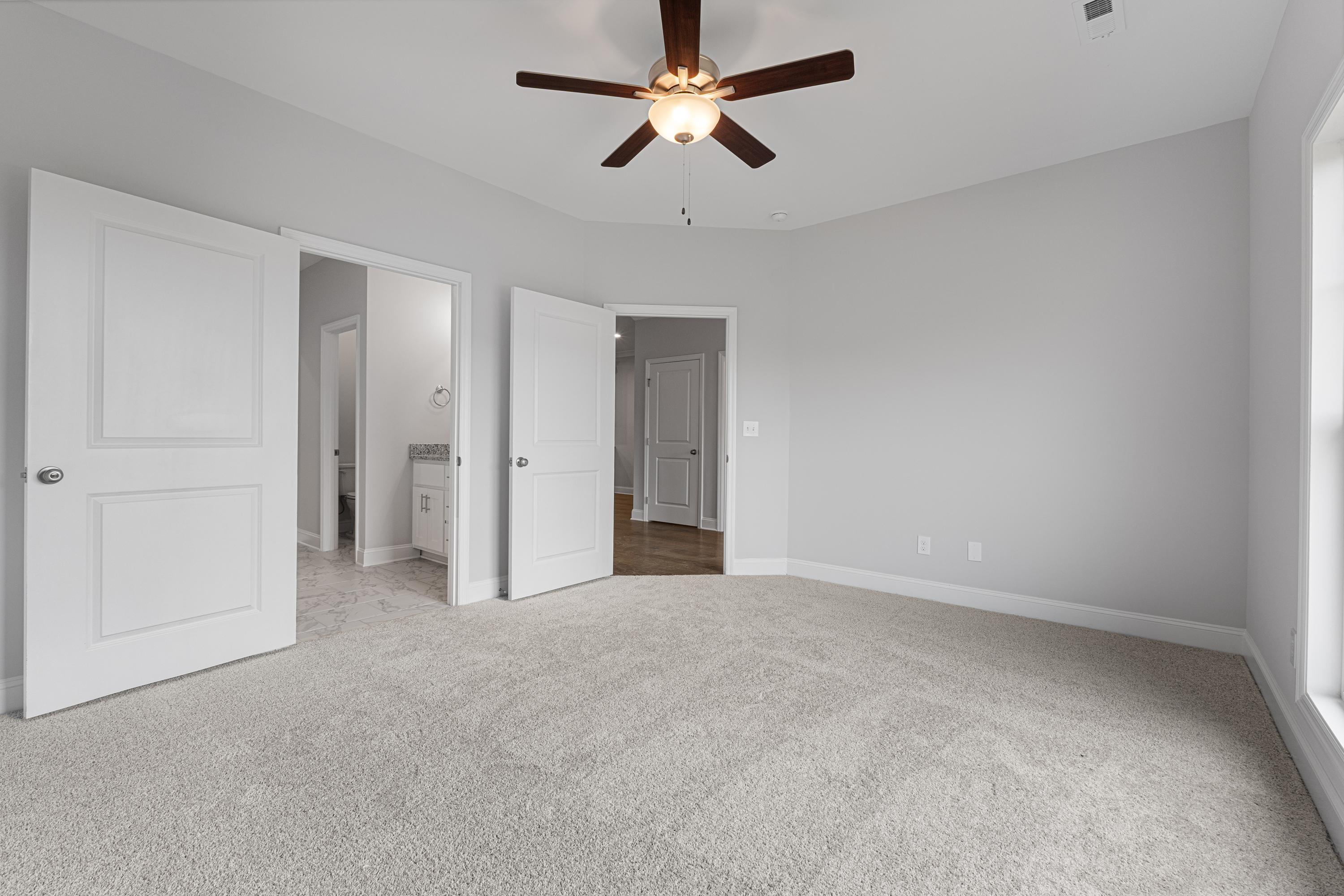 Spacious master bedroom in The Copeland C with gray walls, carpeted floor, ceiling fan, and en-suite bath access