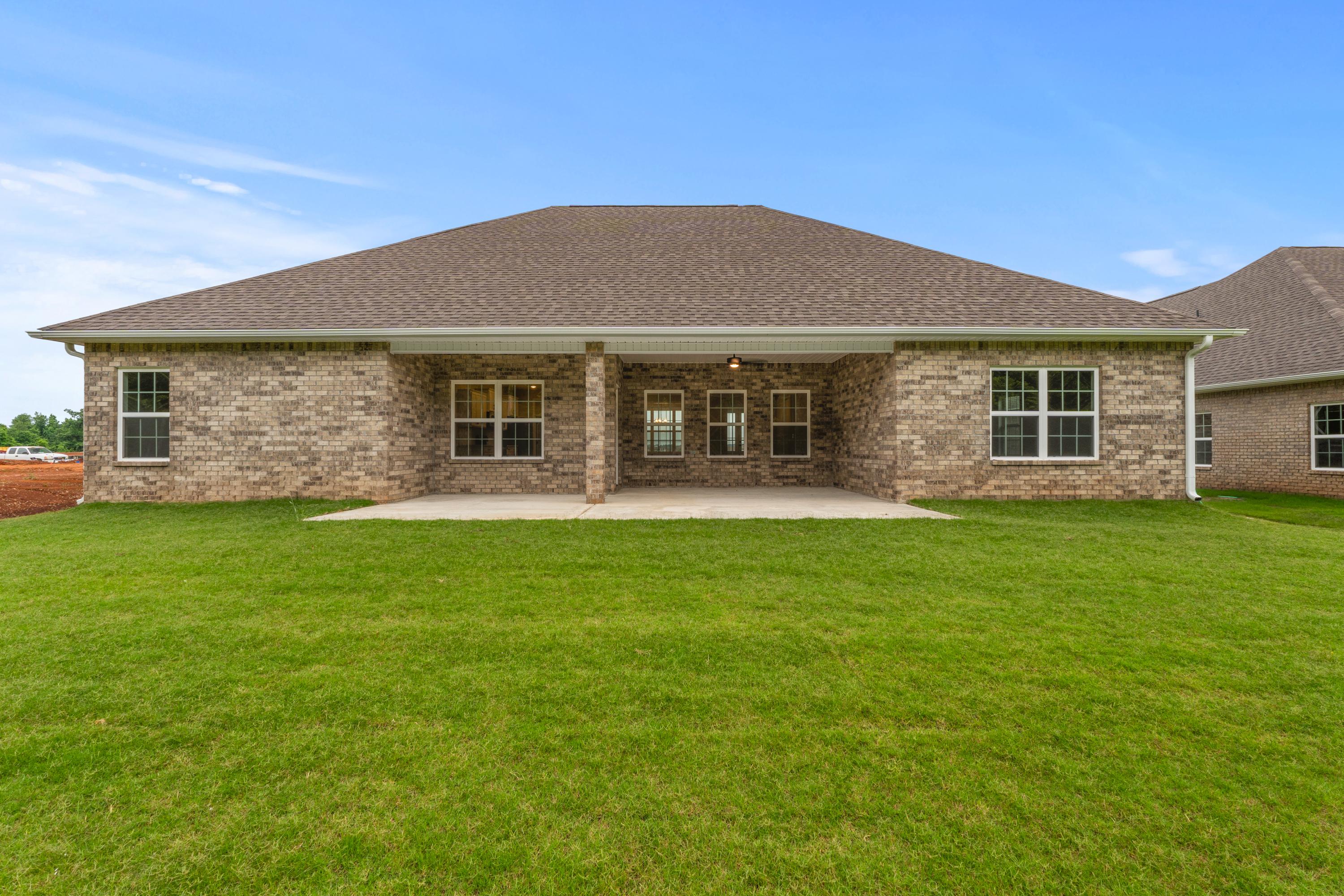 Rear elevation of The Oxford single-story home featuring brick facade, covered patio, and lush green lawn in Meridianville