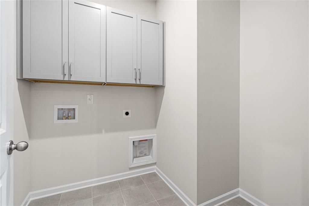Modern laundry room featuring white upper cabinets, washer-dryer hookups, and gray tile flooring in Davidson Homes The Glenwood C at Wehunt Meadows, Hoschton