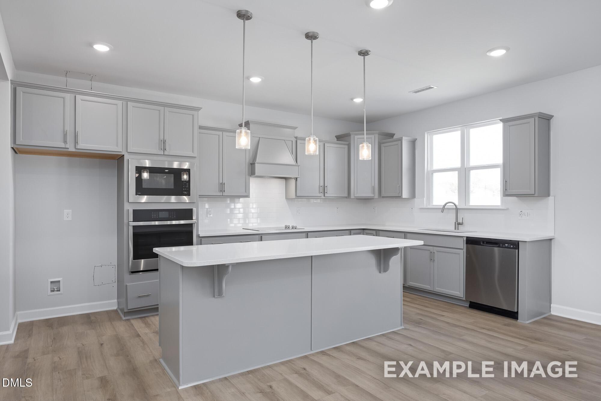 Modern gray kitchen with stainless steel double ovens, large island, and pendant lights in The Hickory II B, Lillington, NC
