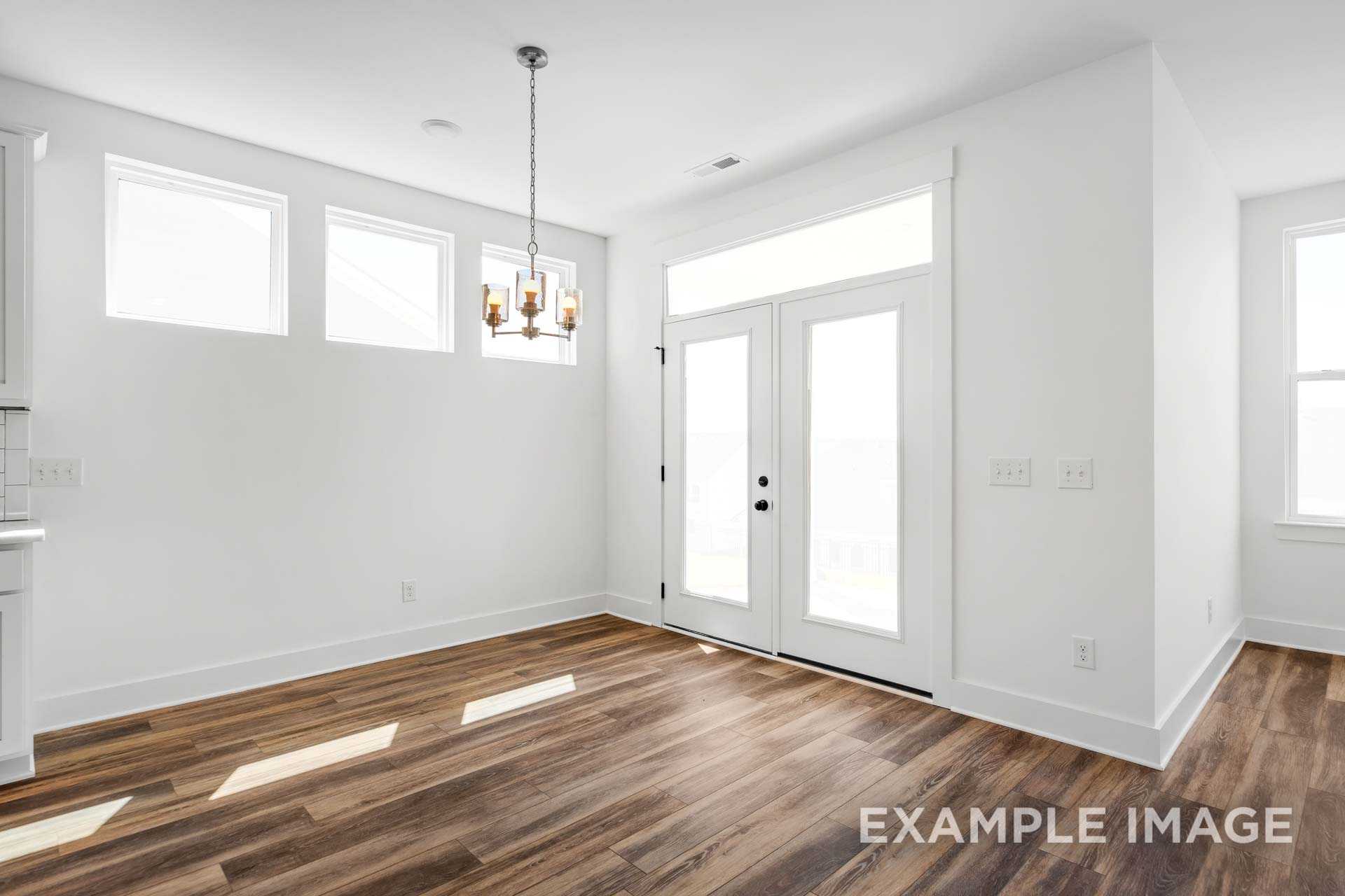 Spacious dining room in The Ash C home with hardwood floors, chandelier, French doors, and large windows