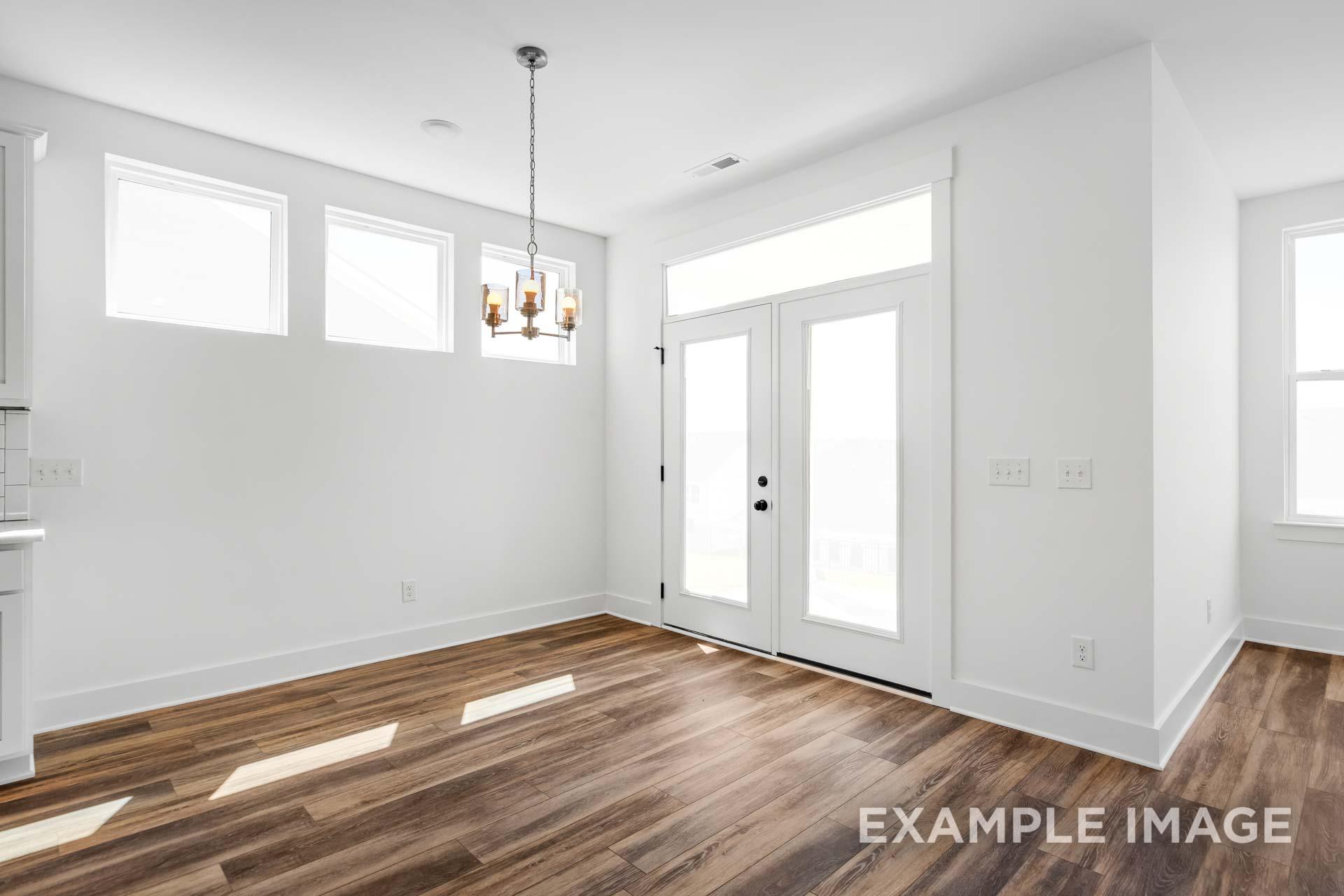 Spacious dining room in The Ash C home with hardwood floors, chandelier, French doors, and large windows
