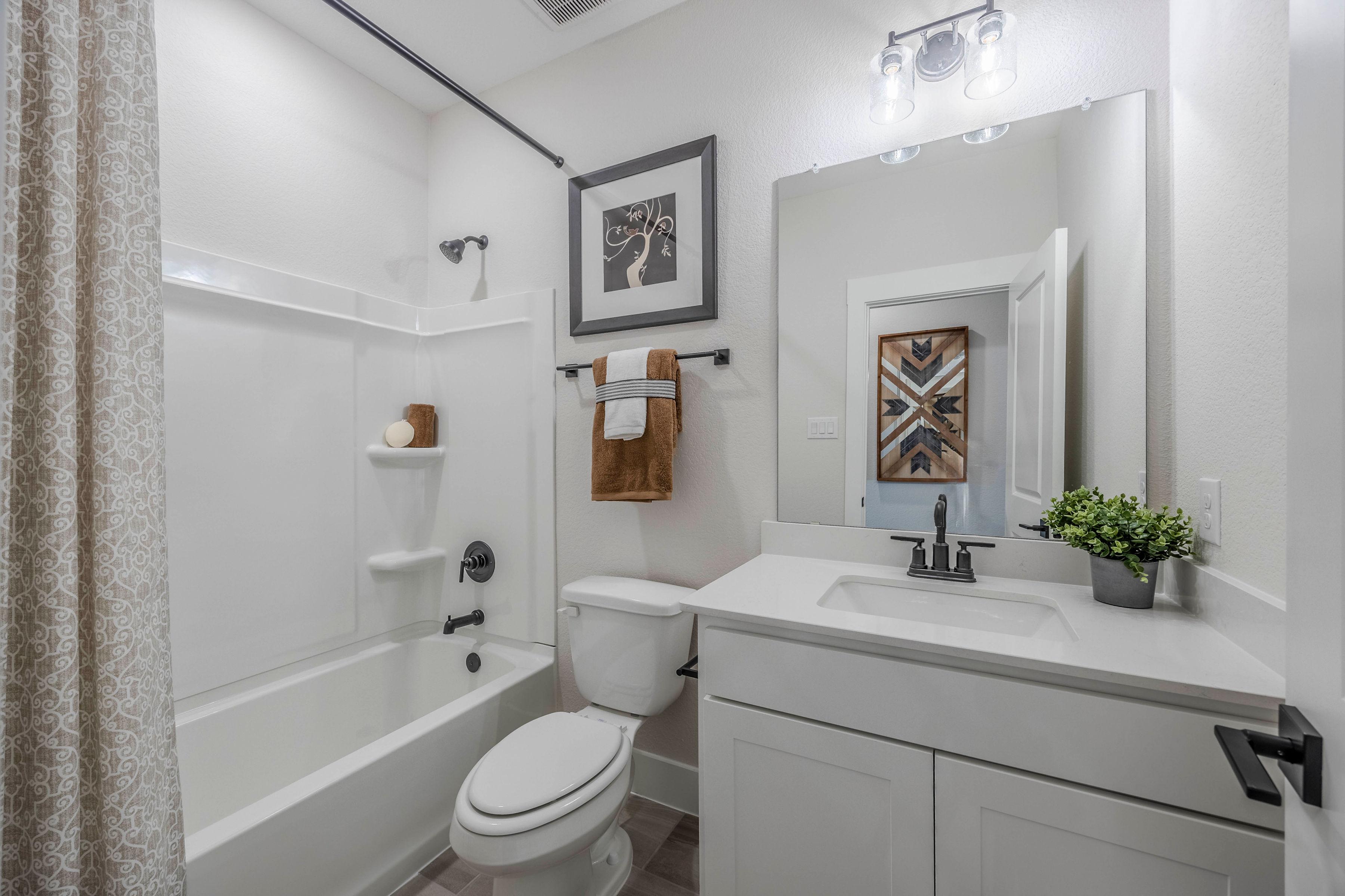 Bright white bathroom with soaking tub, single vanity, large mirror, and modern fixtures at Waverly Estates in Josephine, Texas