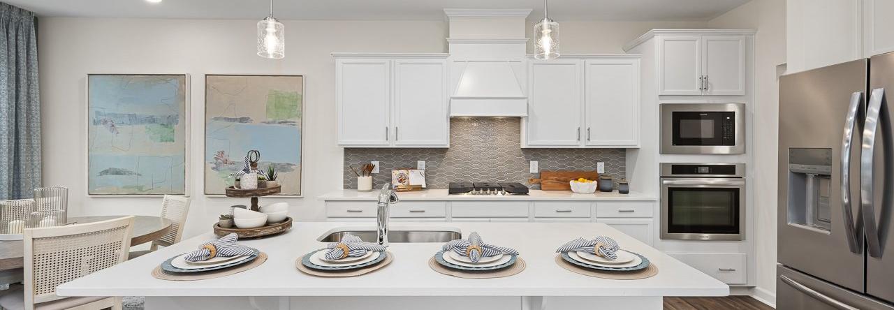 Modern kitchen at Gregory Village Townhomes in Lillington NC with white cabinets, large island, bar stools, and stainless appliances