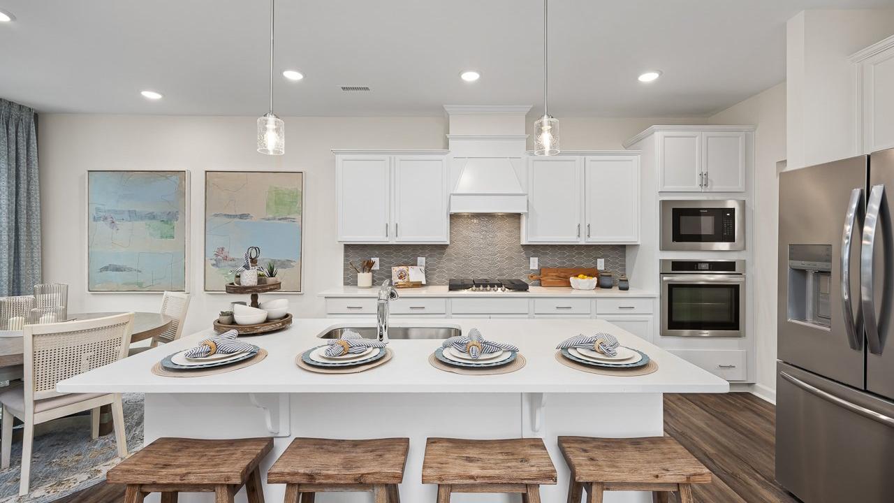 Modern kitchen at Gregory Village Townhomes in Lillington NC with white cabinets, large island, bar stools, and stainless appliances