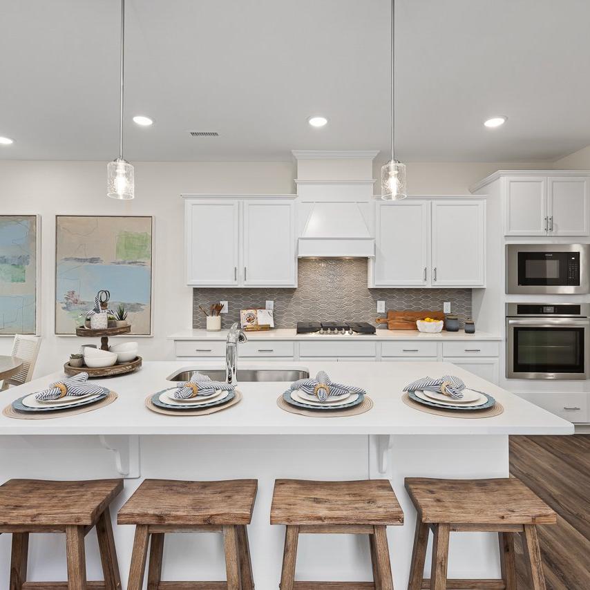 Modern kitchen at Gregory Village Townhomes in Lillington NC with white cabinets, large island, bar stools, and stainless appliances