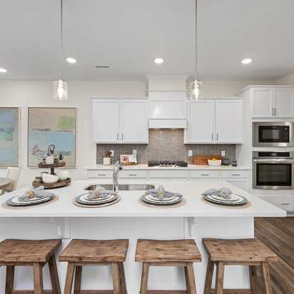 Modern kitchen at Gregory Village Townhomes in Lillington NC with white cabinets, large island, bar stools, and stainless appliances