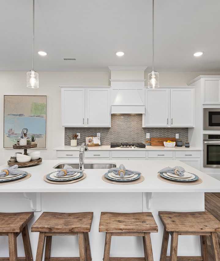 Modern kitchen at Gregory Village Townhomes in Lillington NC with white cabinets, large island, bar stools, and stainless appliances