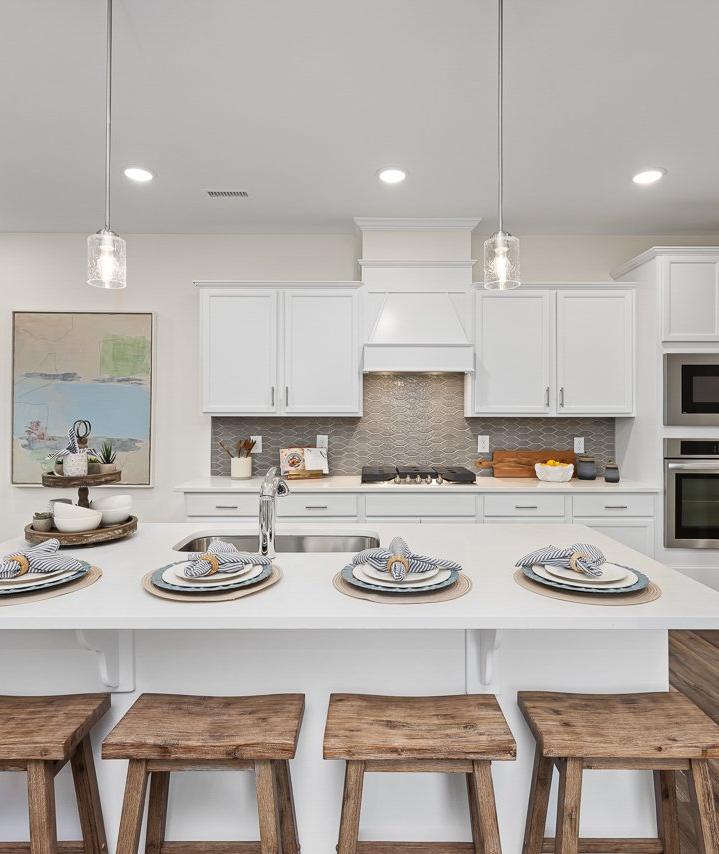 Modern kitchen at Gregory Village Townhomes in Lillington NC with white cabinets, large island, bar stools, and stainless appliances