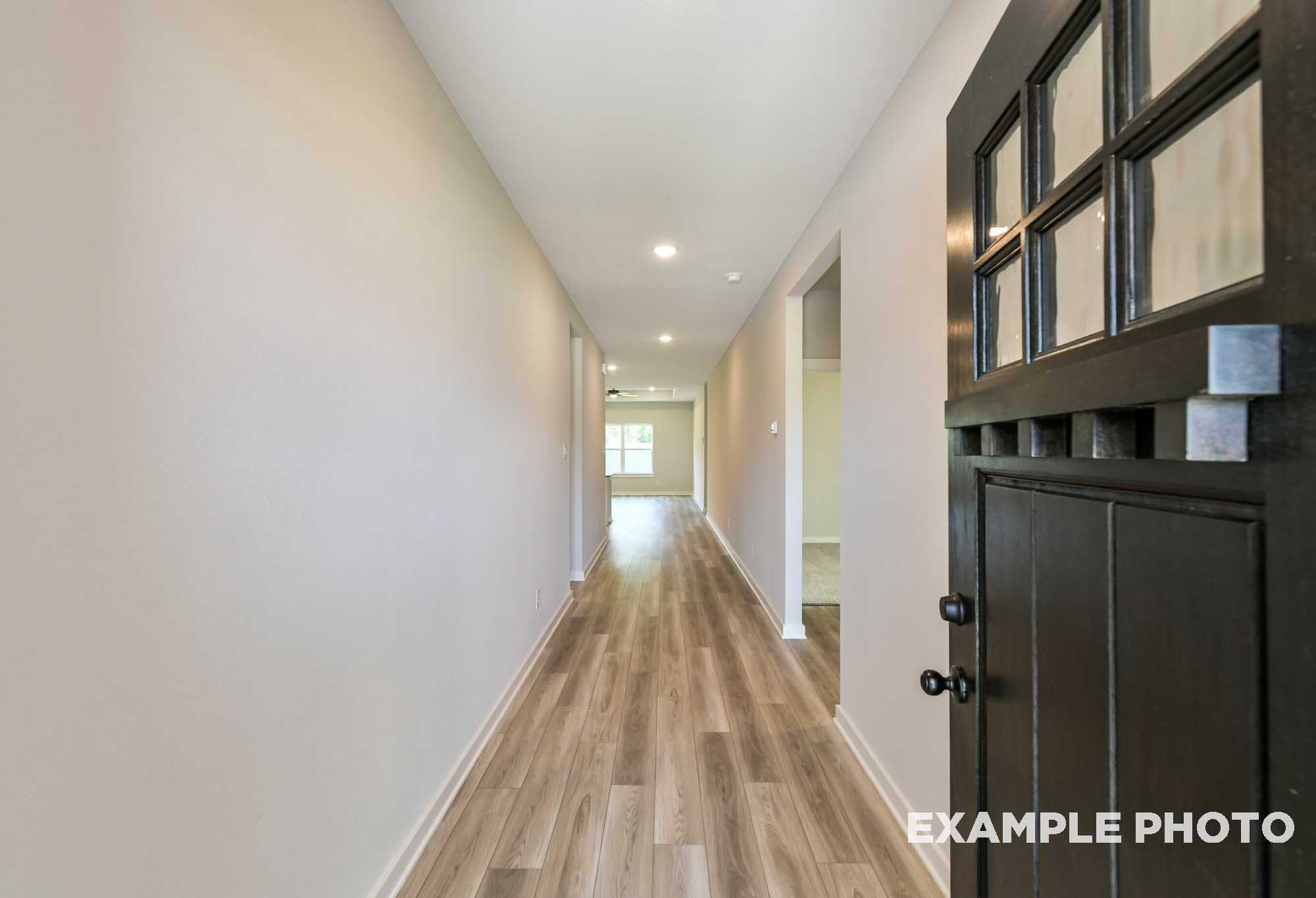 Spacious hallway in The Daphne F home design with neutral walls, wood laminate floors, recessed lights, and dark nine-lite front door