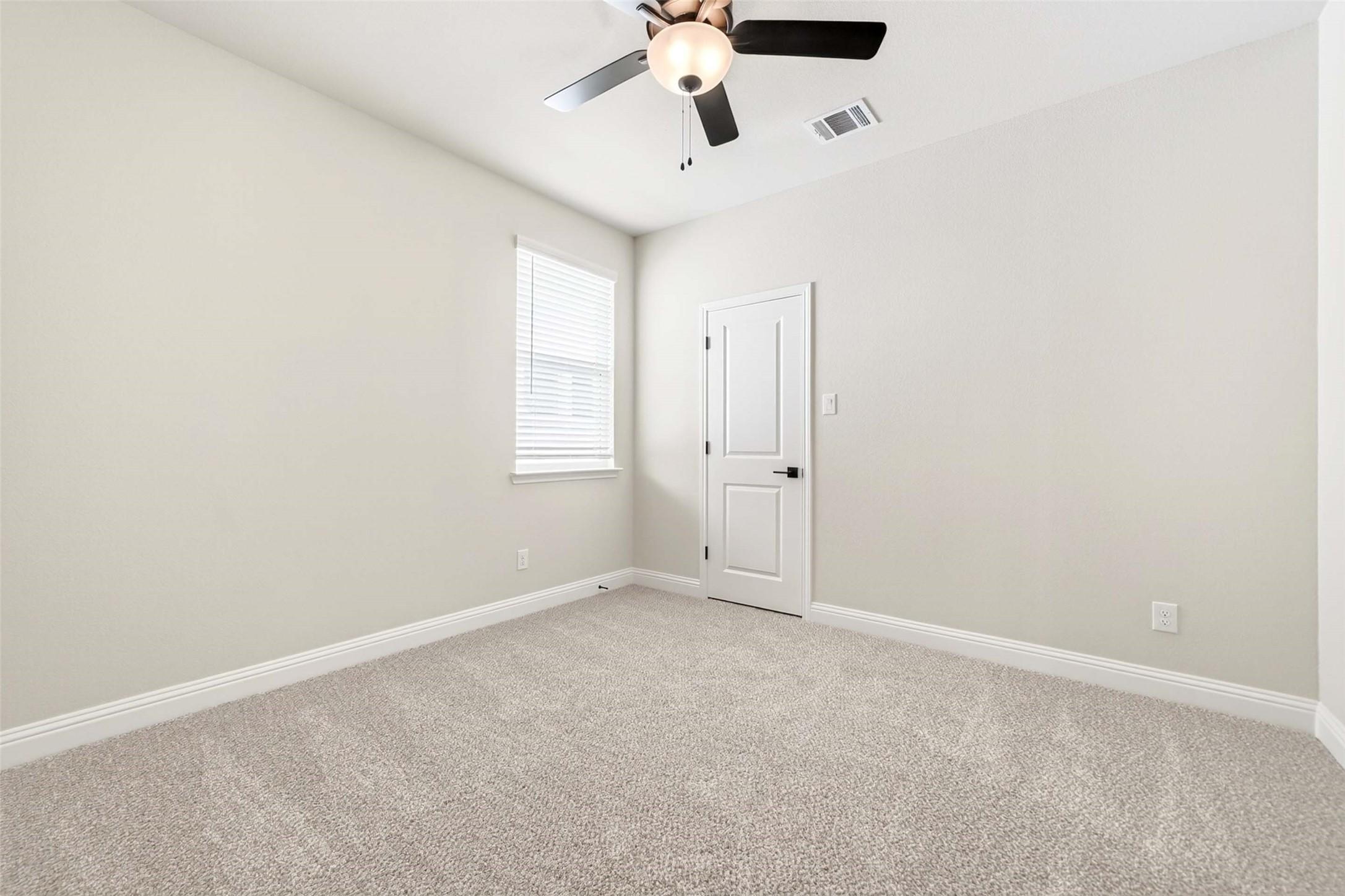 Bright, carpeted bedroom with ceiling fan in The Holly C floor plan at Parks at Foster Crossing in Anna, Texas.