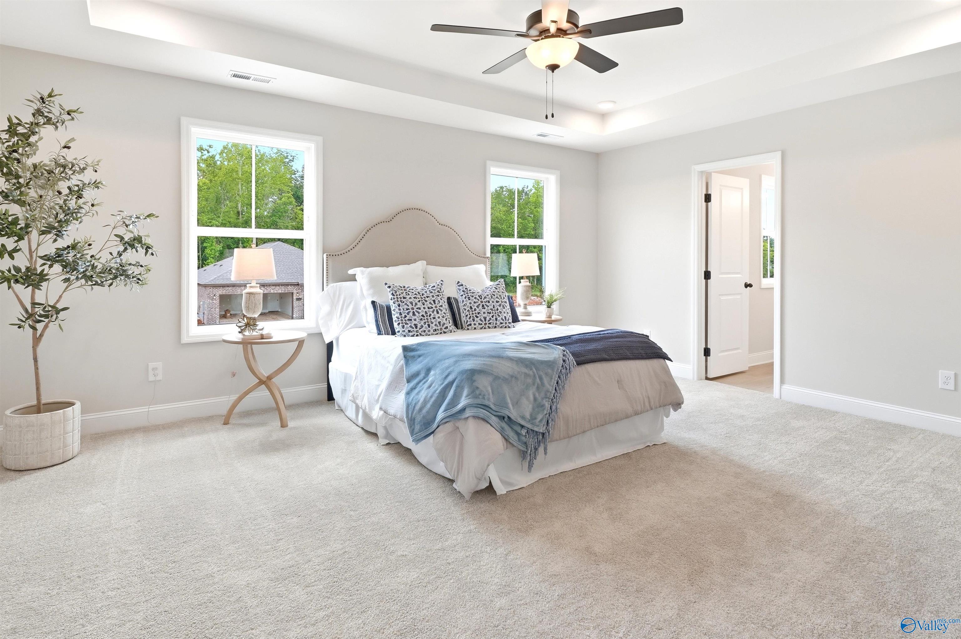 Bright primary bedroom with tray ceiling, ceiling fan, and plush carpet in Davidson Homes The Russell A, Huntsville, AL