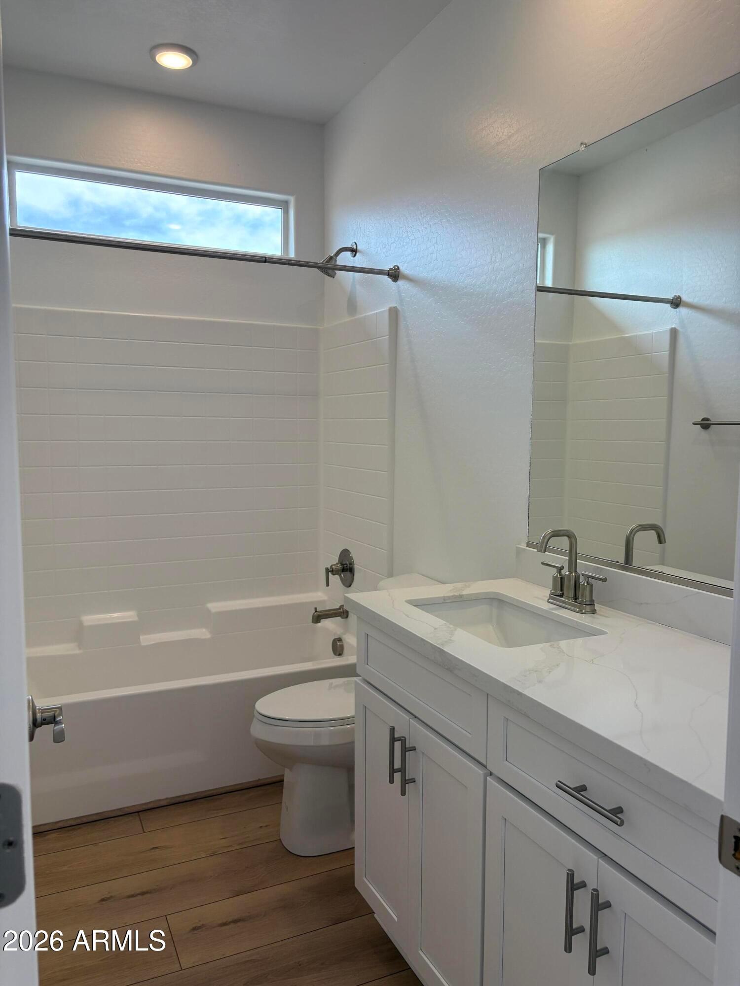Bright bathroom with white vanity, quartz countertop, tub shower combo, and wood-look flooring in Davidson Homes The Evergreen B