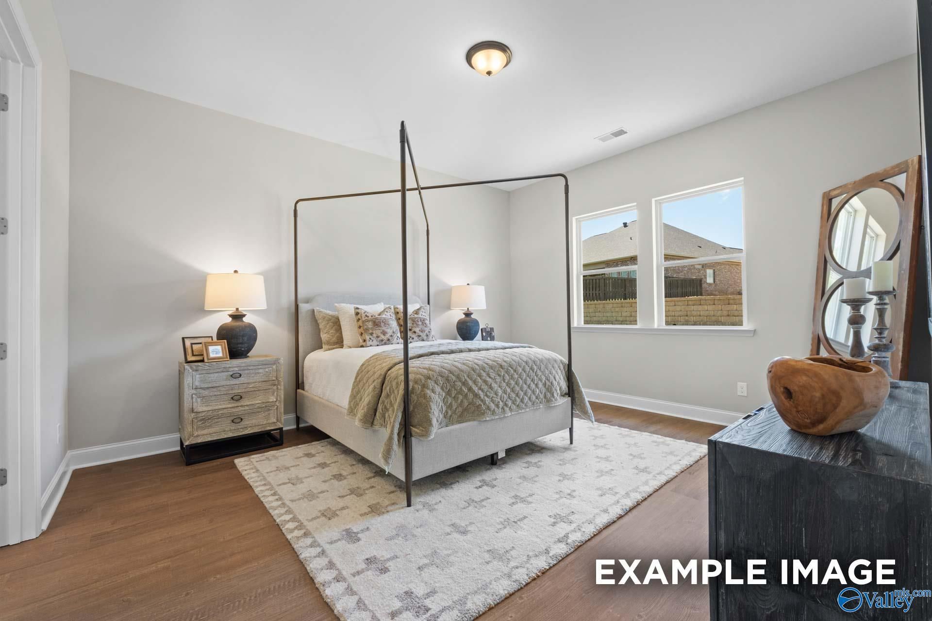 Cozy bedroom with metal four-poster bed, neutral bedding, hardwood floors, and windows overlooking neighborhood in Evermore Homes The Haven E, Owens Cross Roads, Alabama