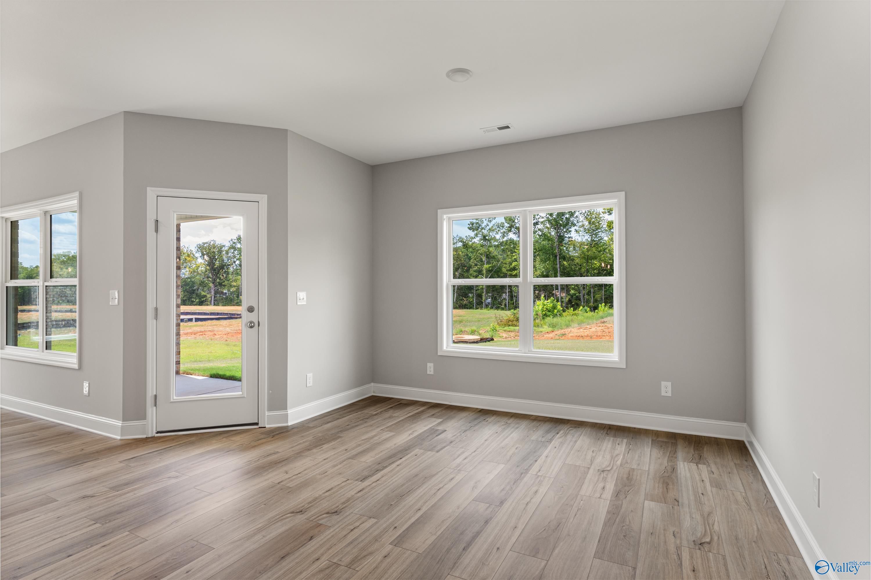 Bright living room with gray walls, large windows to wooded yard, French door, and hardwood floors in The Franklin C, Huntsville, AL