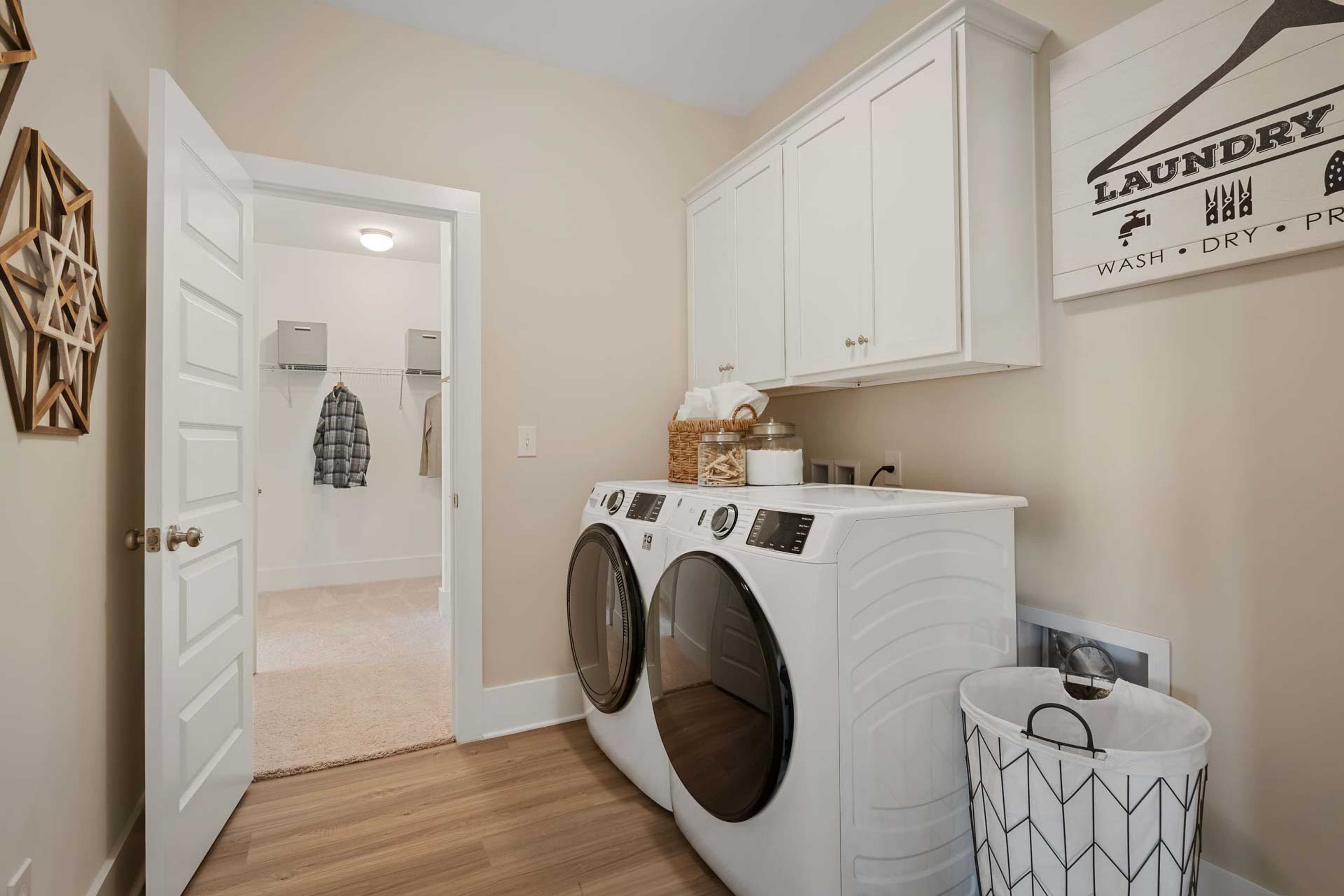 Spacious laundry room at Flint Meadows in New Market, Alabama with white washer dryer, cabinets, hanging rack, and hardwood floors