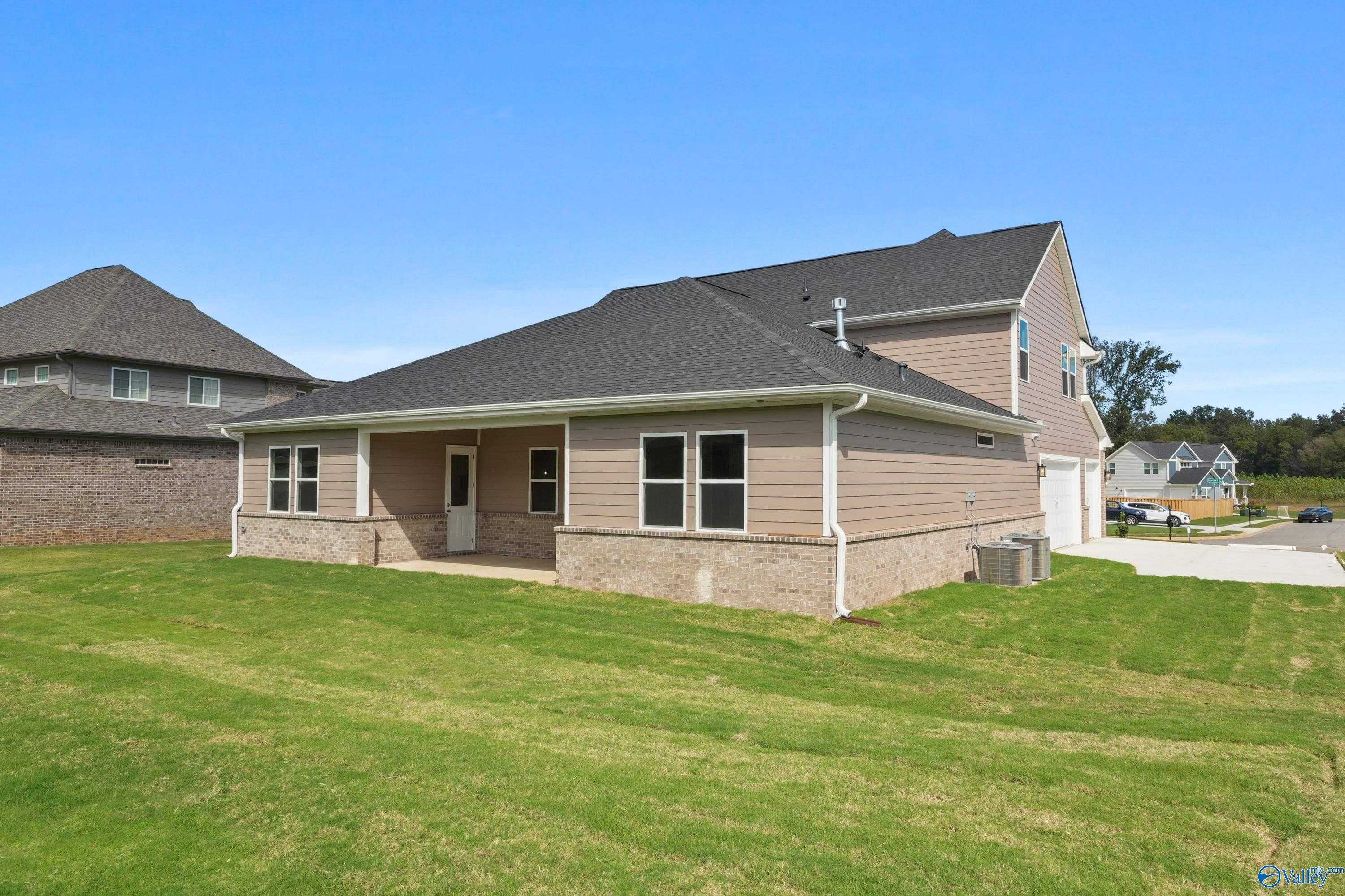 Two-story beige-sided home with 3-car garage, covered porch, and lush lawn in The Meadows at Hampton Cove, Owens Cross Roads, AL