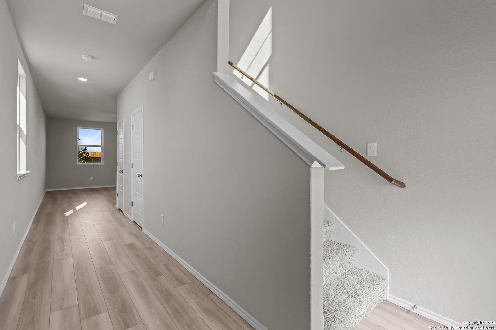 Bright hallway with light wood floors, gray walls, and carpeted staircase in The Trinity D 4-bedroom home, Applewhite Meadows, San Antonio