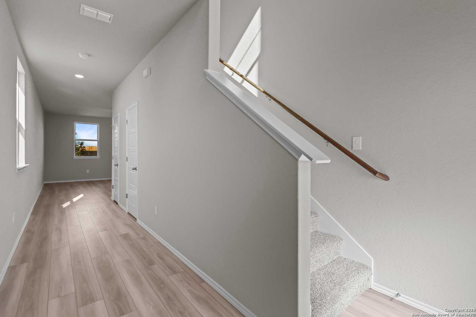 Bright hallway with light wood floors, gray walls, and carpeted staircase in The Trinity D 4-bedroom home, Applewhite Meadows, San Antonio