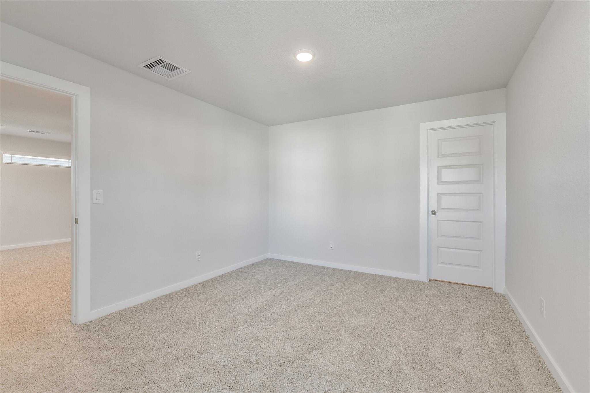 Spacious empty bedroom with beige carpet, white walls, and paneled doors in Davidson Homes The Rio Grande H, Magnolia, Texas